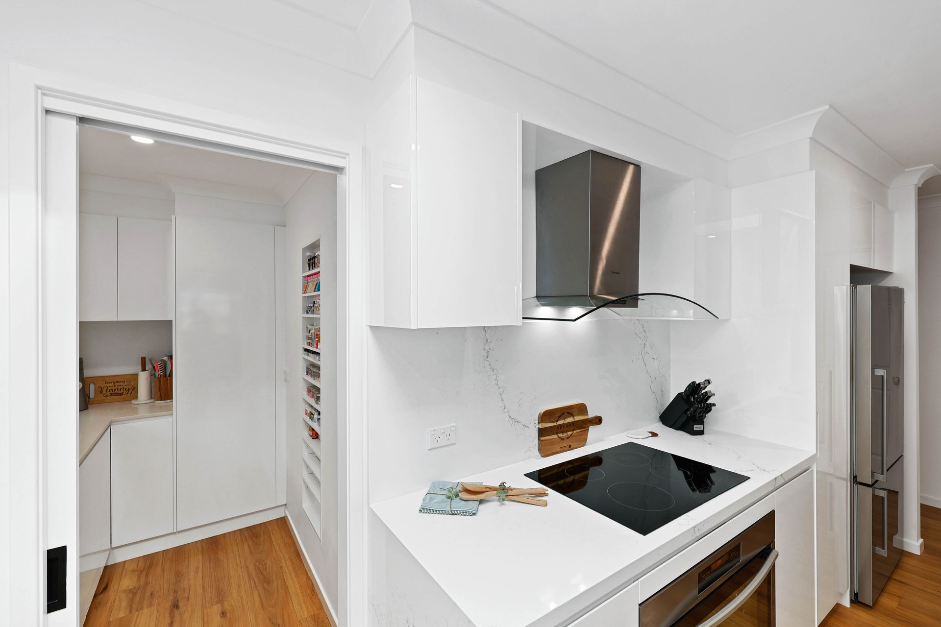 Bright White Modern Kitchen with Wood Floors, Stainless Hood and Black Cooktop — Above & Beyond Interiors in Smeaton Grange, NSW