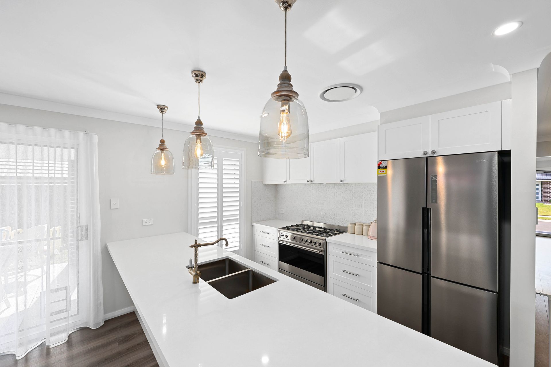 A Kitchen with Island, Pendant Lights, Stainless Steel Fridge, and Gas Range — Above & Beyond Interiors in Smeaton Grange, NSW