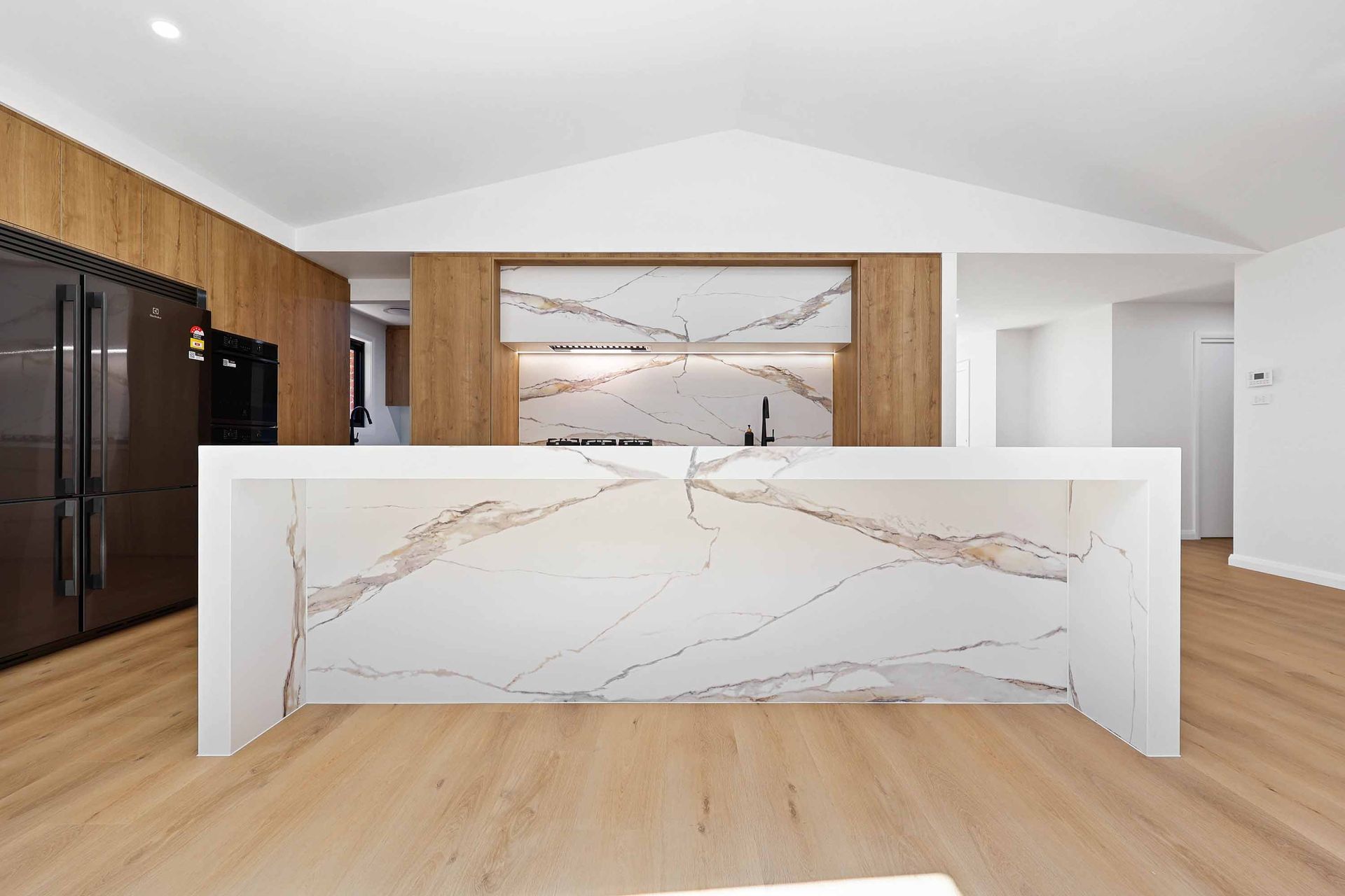 A Kitchen with Marble Island, Wood Cabinets, and Black Appliances — Above & Beyond Interiors in Smeaton Grange, NSW