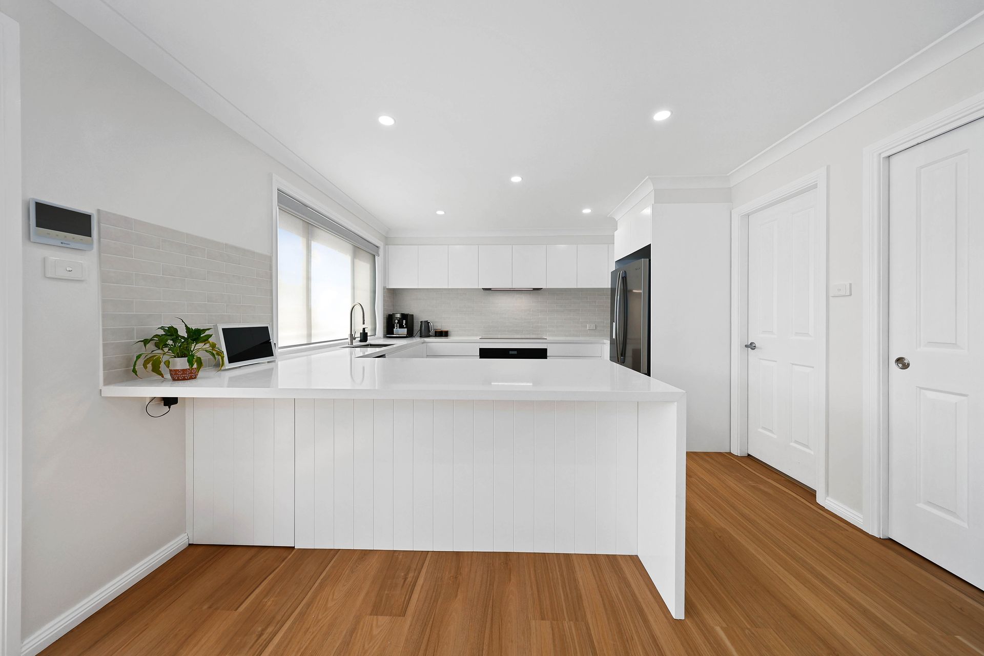 Bright Modern White Kitchen with Wood Floors and Island Counter — Above & Beyond Interiors in Smeaton Grange, NSW