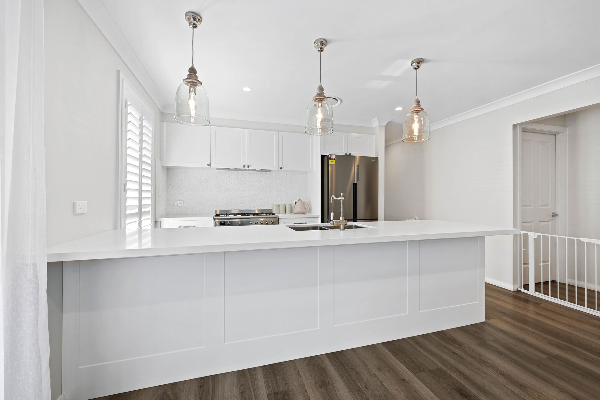 A Modern White Kitchen with Island, Stainless Fridge, and Wood Floors — Above & Beyond Interiors in Smeaton Grange, NSW
