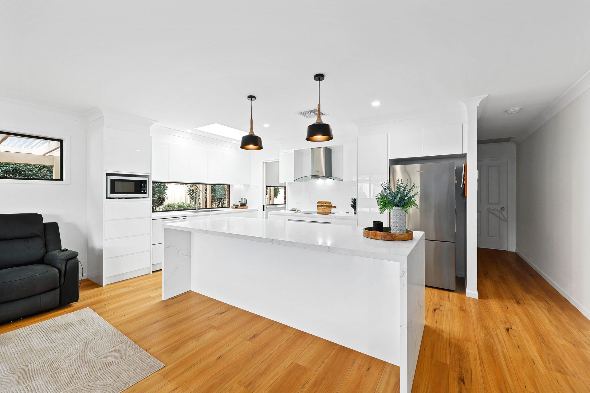 Bright Open Kitchen with Black Pendant Lights, Stainless Fridge, and Wood Floors — Above & Beyond Interiors in Smeaton Grange, NSW