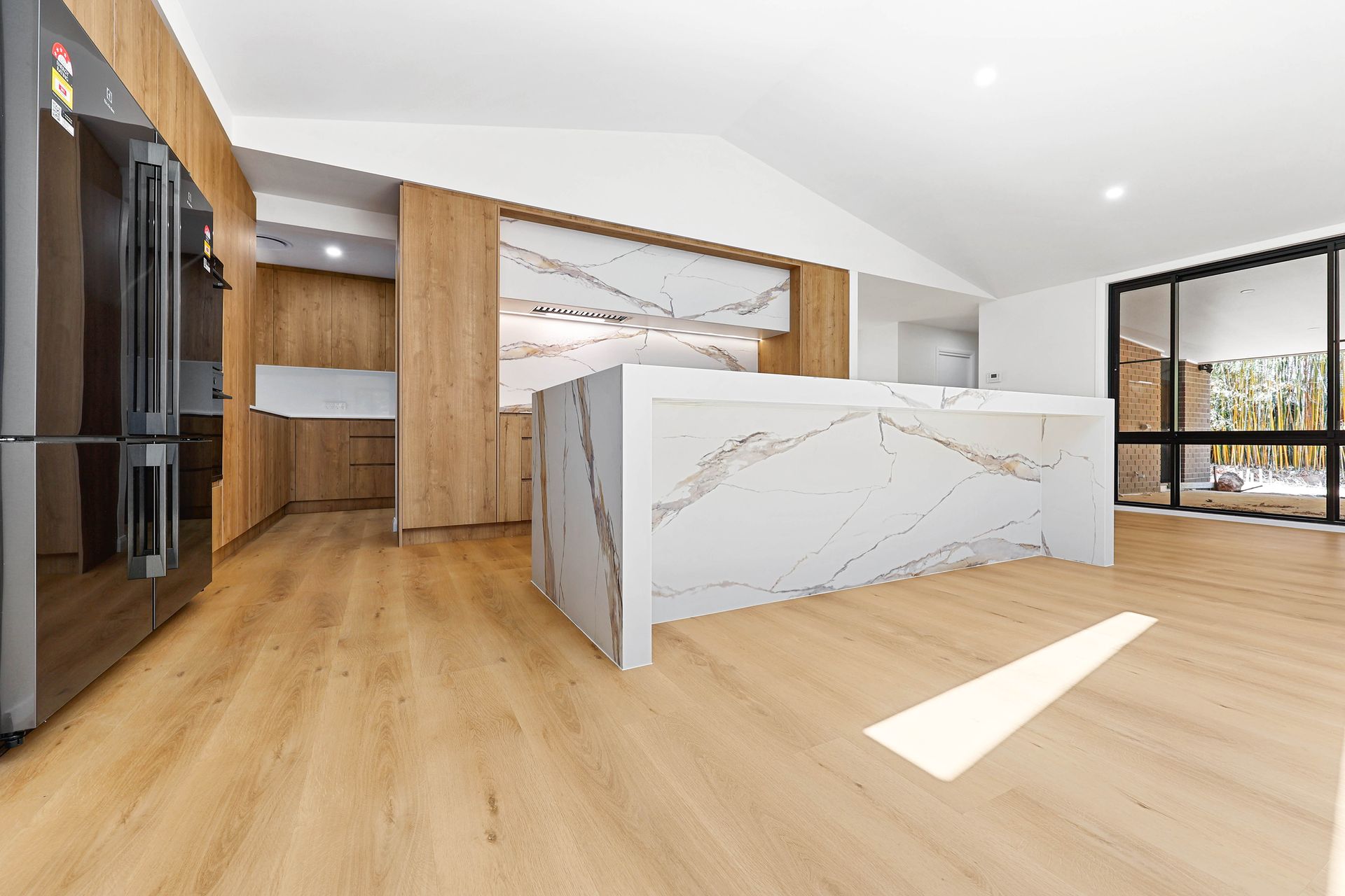 A Kitchen with Light Wood Floors, Marble Island, Black Fridge, and Large Windows — Above & Beyond Interiors in Smeaton Grange, NSW