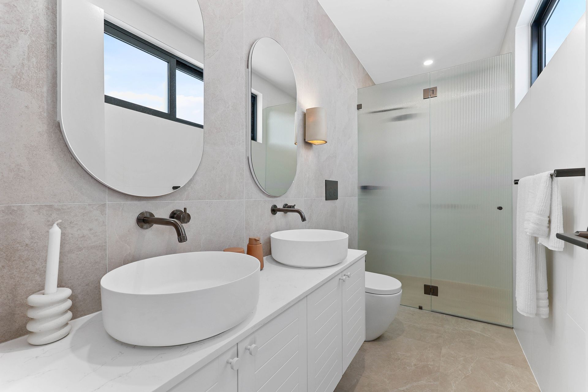 Modern bathroom with two sinks, oval mirrors, and a glass shower — Above & Beyond Interiors in Southern Highlands, NSW