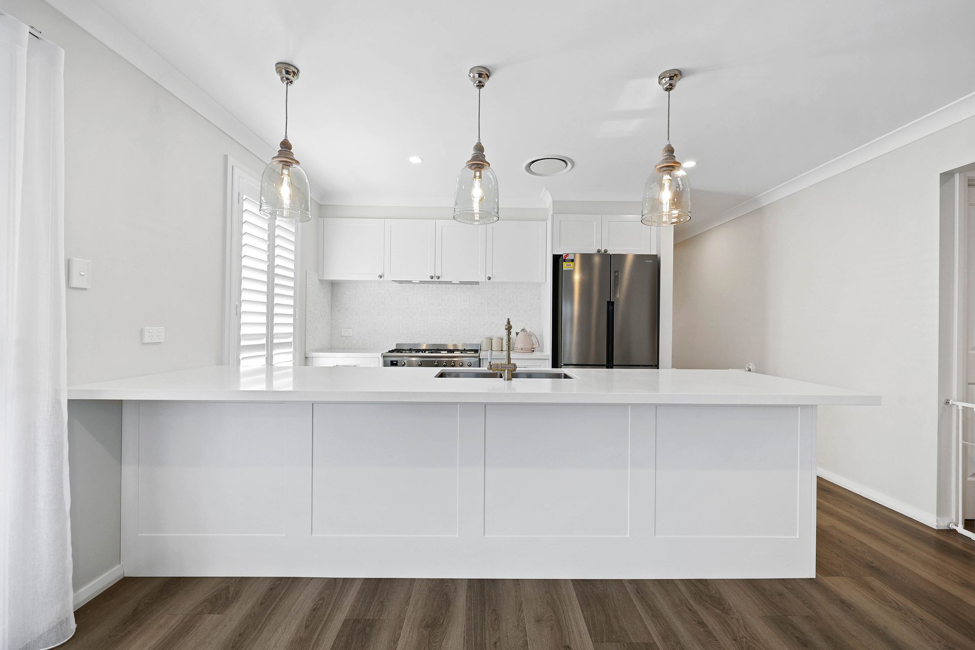 A Modern Kitchen with Stainless Appliances, Pendant Lights, and Wood Flooring — Above & Beyond Interiors in Smeaton Grange, NSW