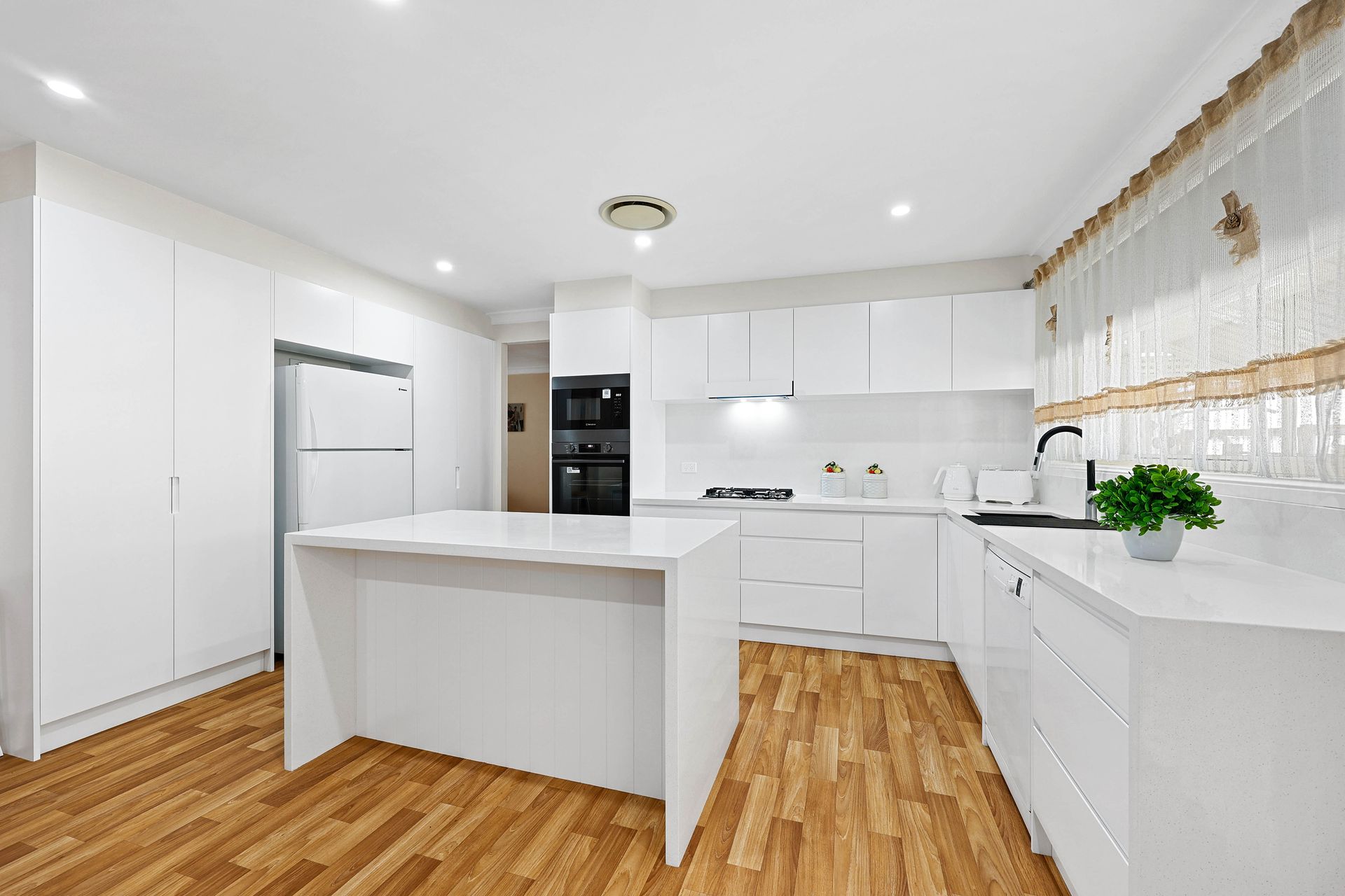 A Modern White Kitchen with Wood Floors — Above & Beyond Interiors in Smeaton Grange, NSW