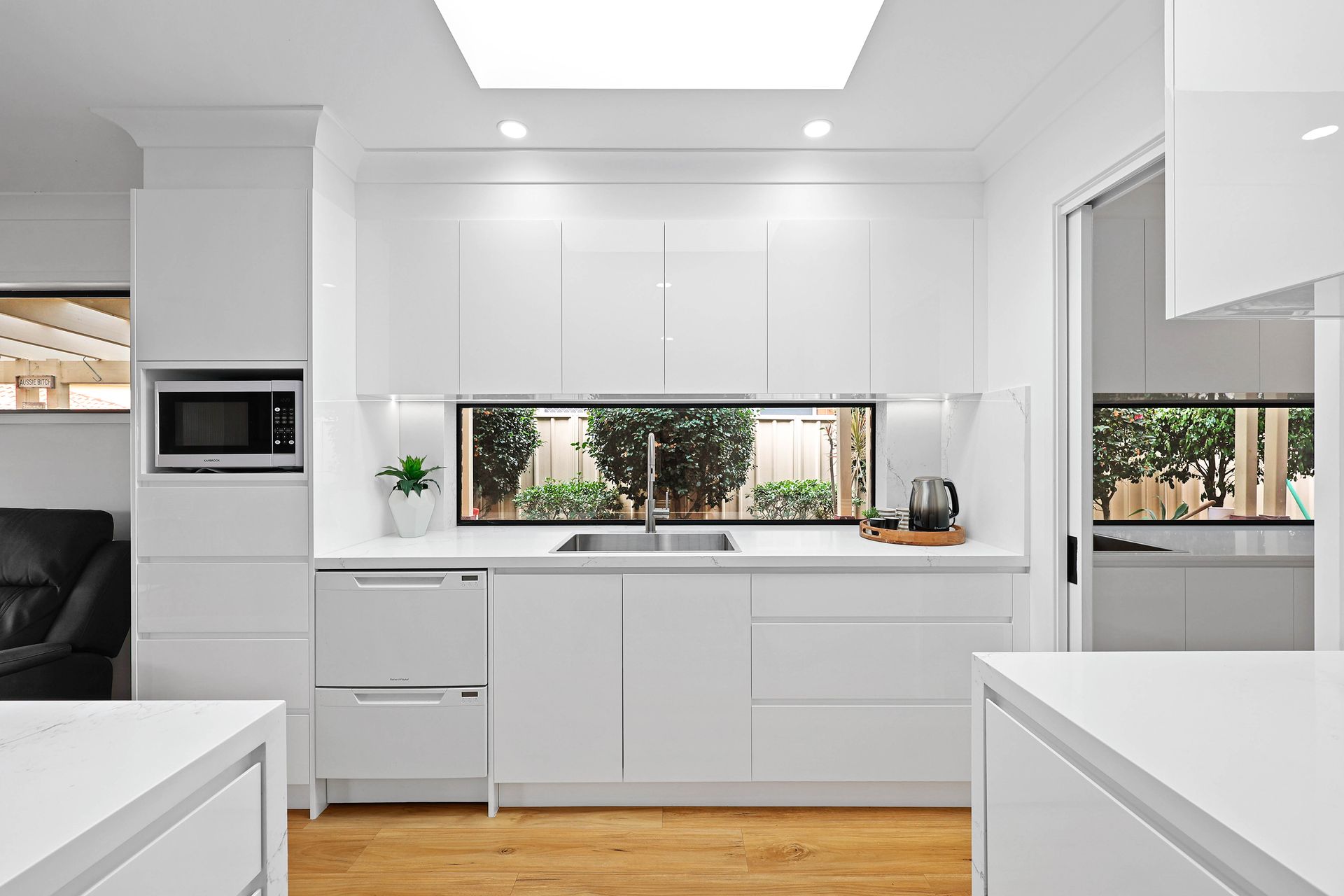 Modern White Kitchen with Sink Under Window, Built-In Oven, and Light Wood Floor — Above & Beyond Interiors in Smeaton Grange, NSW