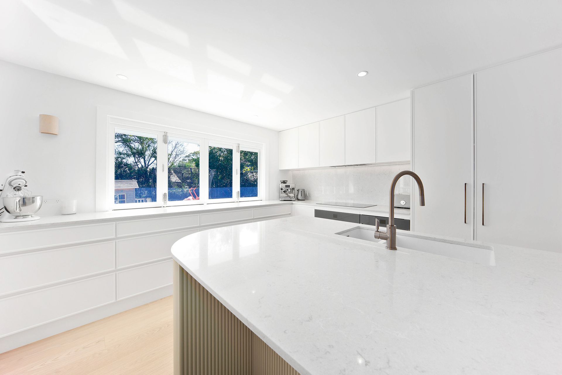 White Modern Kitchen With Curved Countertop — Above & Beyond Interiors in Smeaton Grange, NSW