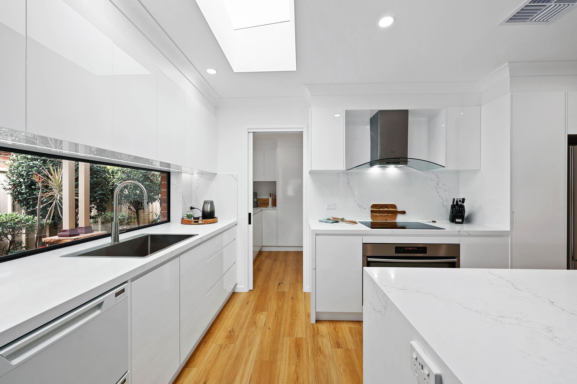 Bright Modern White Kitchen with Wood Floors and Stainless Steel Appliances — Above & Beyond Interiors in Smeaton Grange, NSW