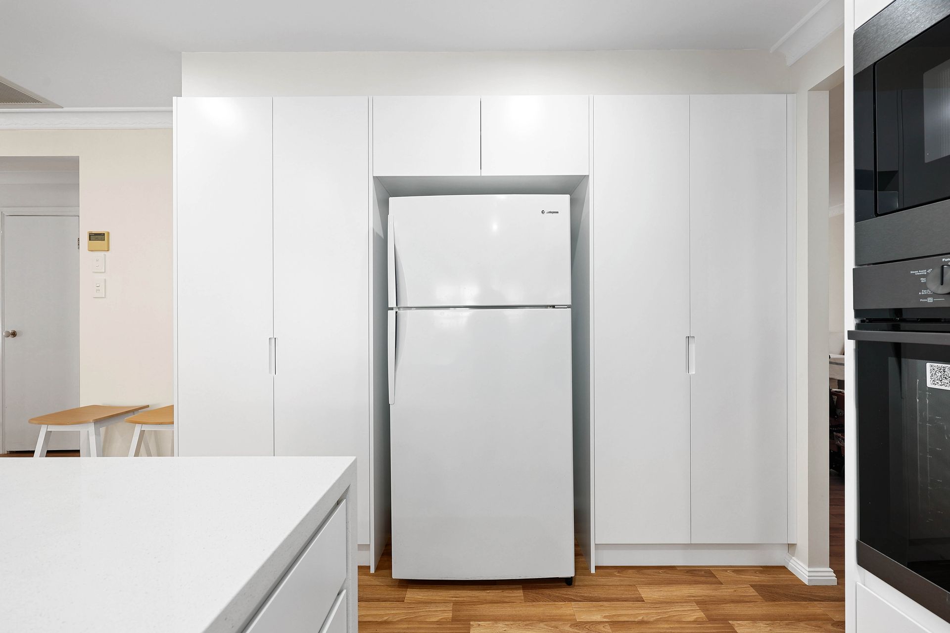 Modern White Kitchen with A Stainless-Steel Refrigerator — Above & Beyond Interiors in Smeaton Grange, NSW