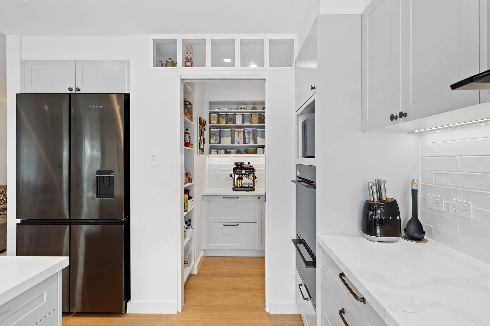 Bright White Galley Kitchen with Stainless Fridge — Above & Beyond Interiors in Smeaton Grange, NSW
