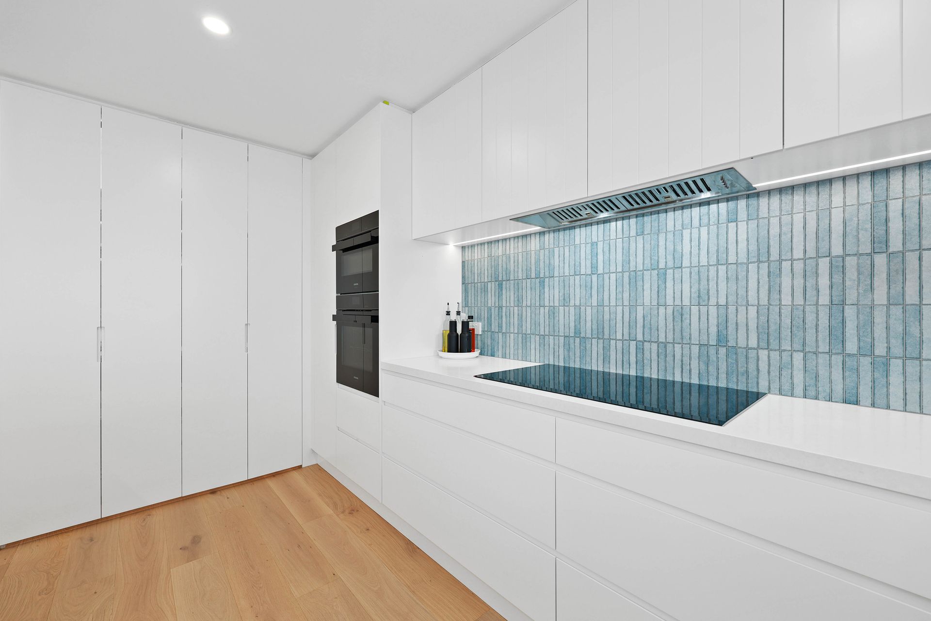 Modern White Kitchen with Wood Floor and Blue-Tiled Backsplash — Above & Beyond Interiors in Smeaton Grange, NSW