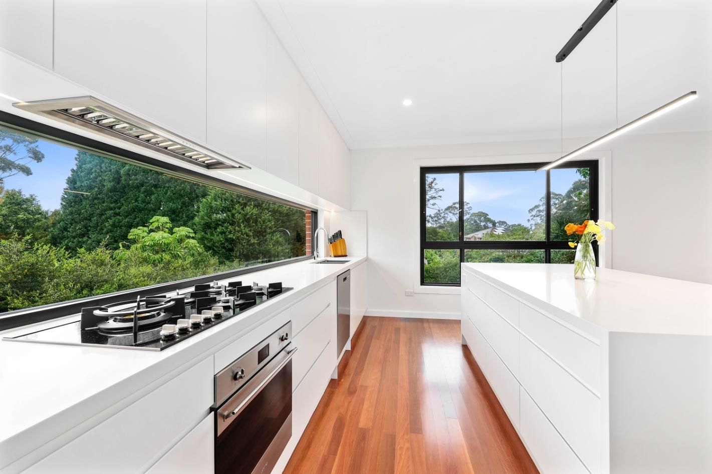 Bright Modern Kitchen with White Cabinets and Wood Floors — Above & Beyond Interiors in Smeaton Grange, NSW