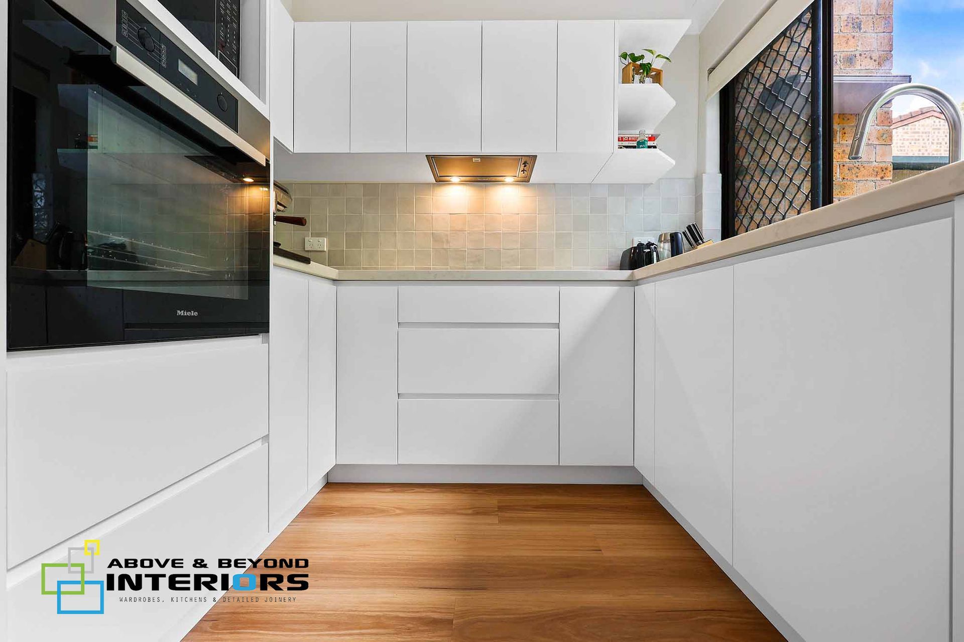 Modern White Kitchen with Wood Floors, Built-In Oven, and Tiled Backsplash — Above & Beyond Interiors in Smeaton Grange, NSW