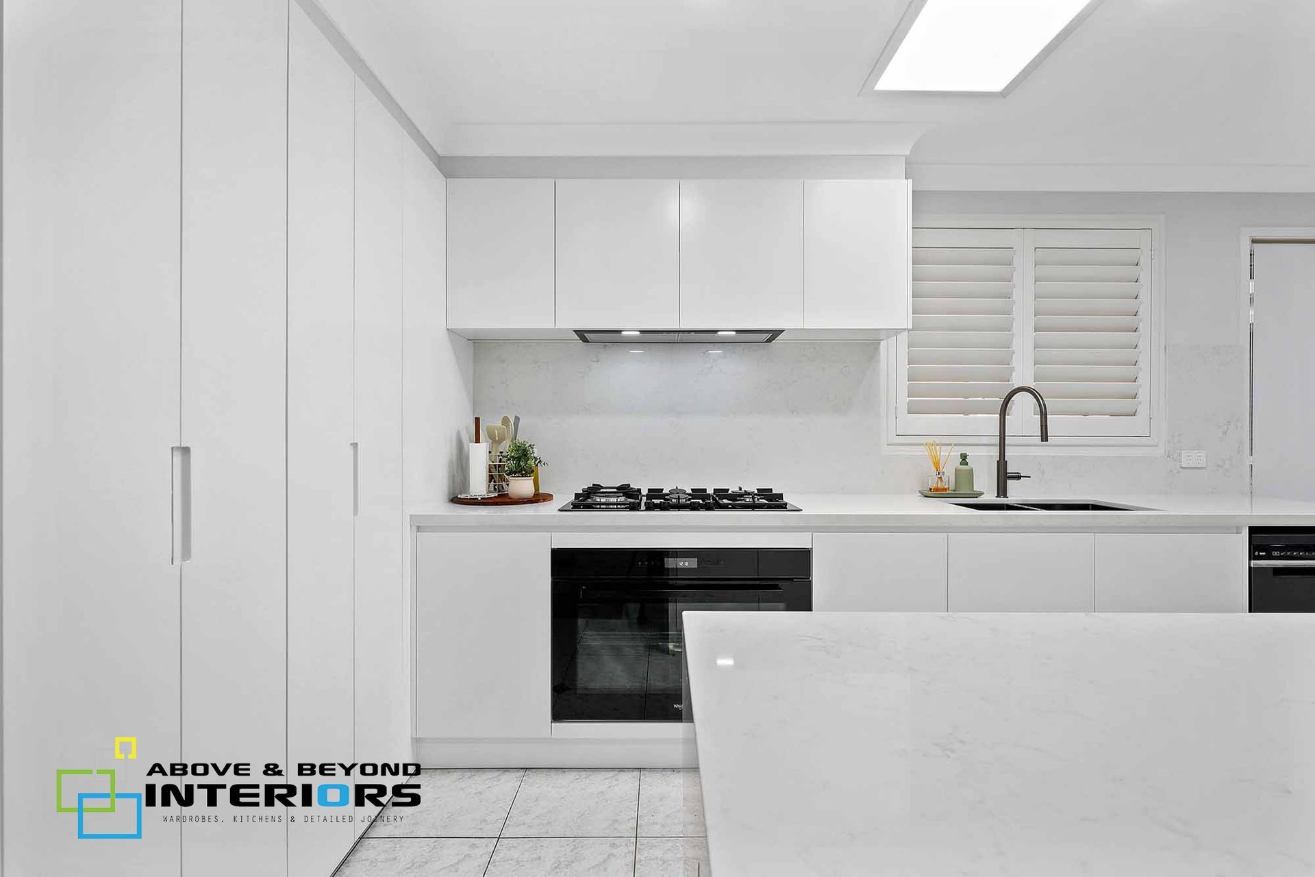 Bright White Modern Kitchen with Island, Built-In Oven, Black Faucet, and Tiled Floor — Above & Beyond Interiors in Smeaton Grange, NSW