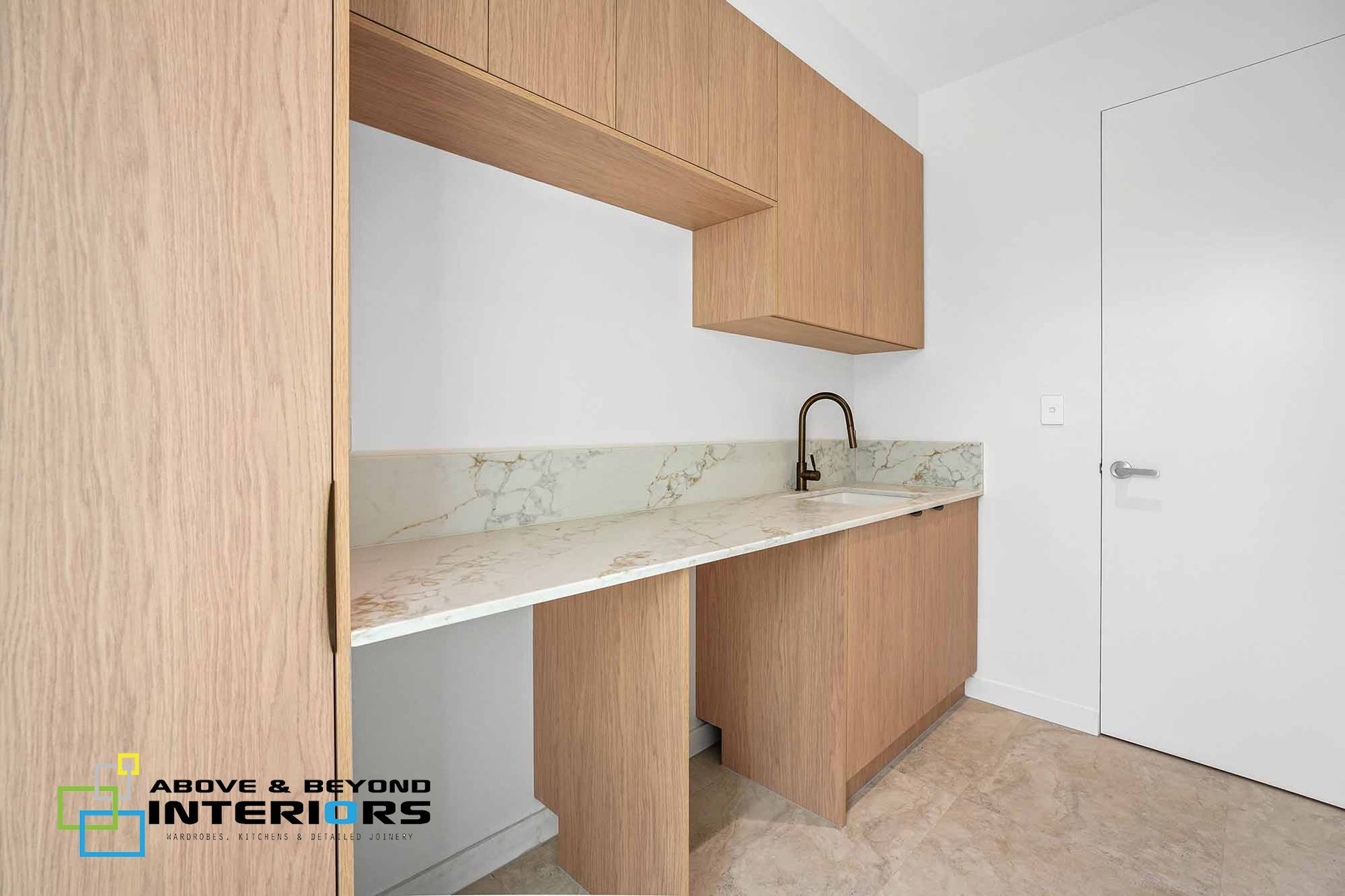 Modern Kitchen Nook with Light Wood Cabinets and Sink Beside a White Door — Above & Beyond Interiors in Smeaton Grange, NSW