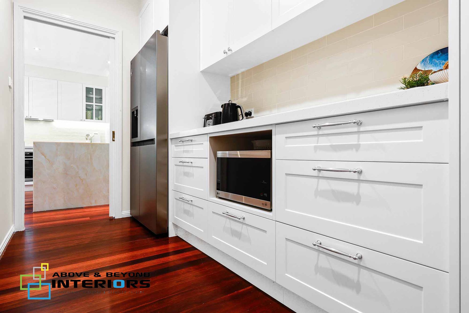 Bright Modern Kitchen with White Cabinets, Stainless Fridge, and Wood Floor — Above & Beyond Interiors in Smeaton Grange, NSW