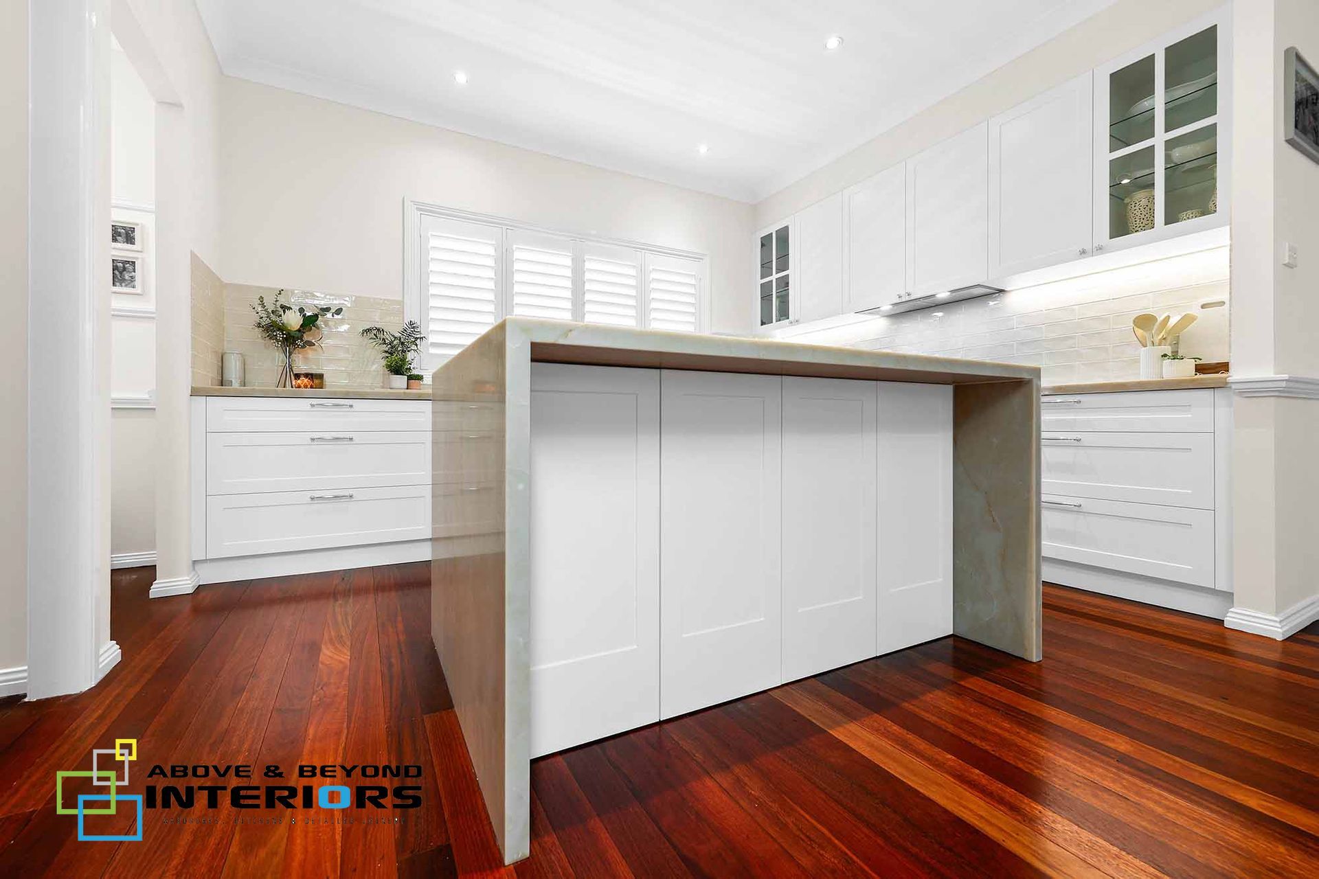 Bright White Kitchen with A Large Island, White Cabinets, and Warm Wood Floors — Above & Beyond Interiors in Smeaton Grange, NSW