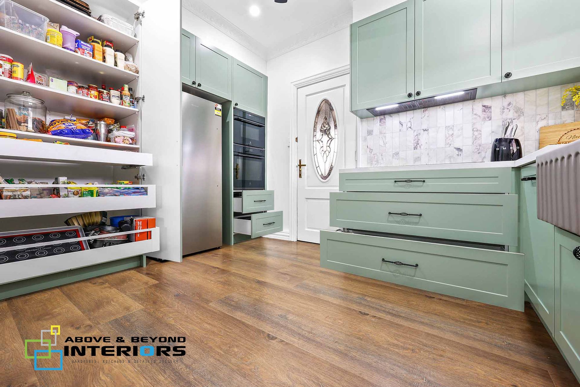 A Kitchen with Mint Cabinets, Wood Floor, Stainless Fridge, and A Spice Rack Shelf — Above & Beyond Interiors in Smeaton Grange, NSW