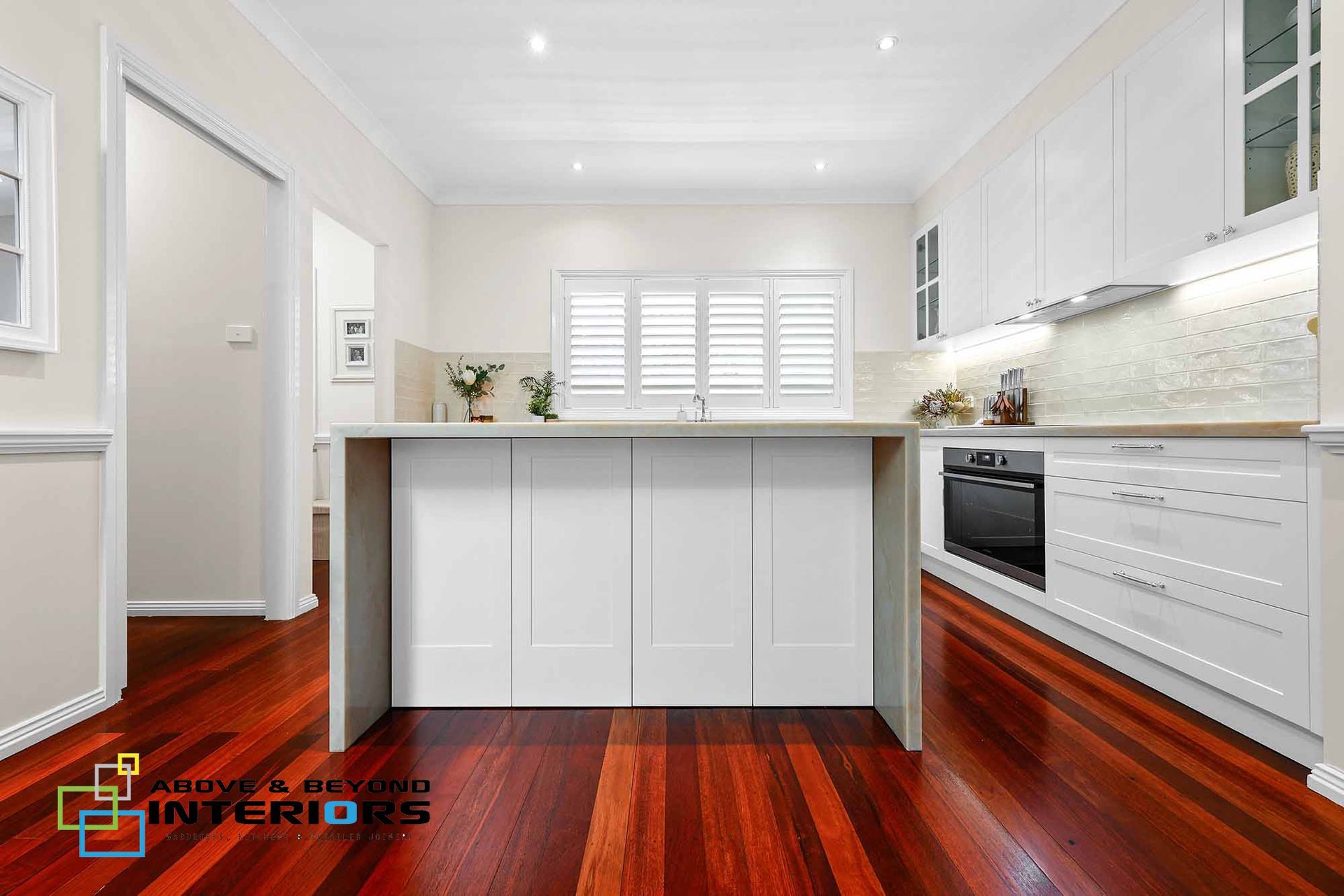 Bright Modern White Kitchen with Island, Built-In Oven, and Glossy Red Wood Floors — Above & Beyond Interiors in Smeaton Grange, NSW