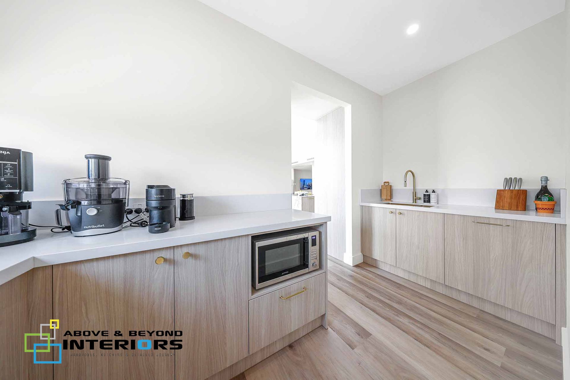 A Kitchen with Wood Cabinetry, White Countertops, and Appliances — Above & Beyond Interiors in Smeaton Grange, NSW