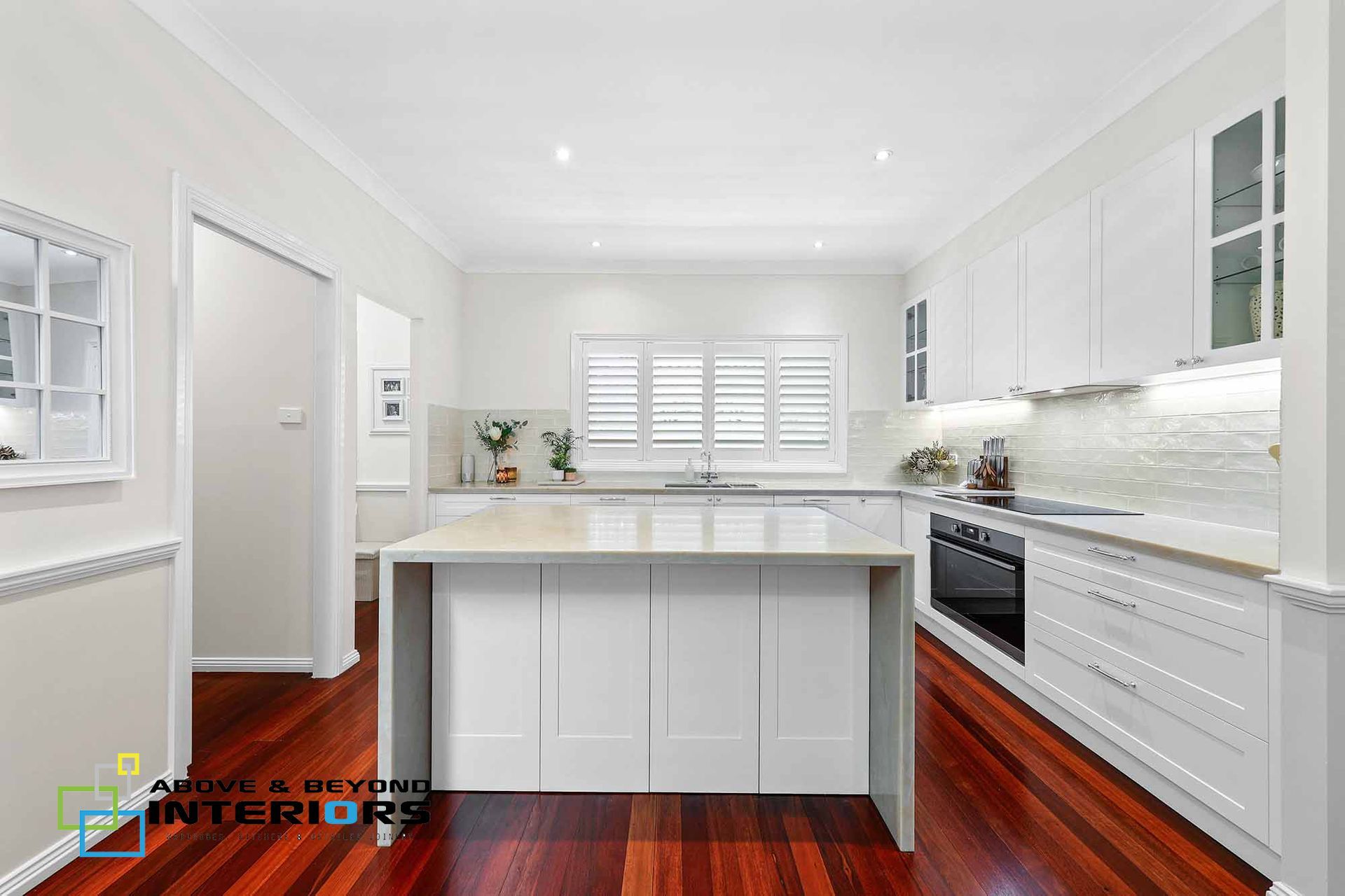 Bright White Modern Kitchen with Island, Stainless Oven, and Reddish Wood Floors — Above & Beyond Interiors in Smeaton Grange, NSW