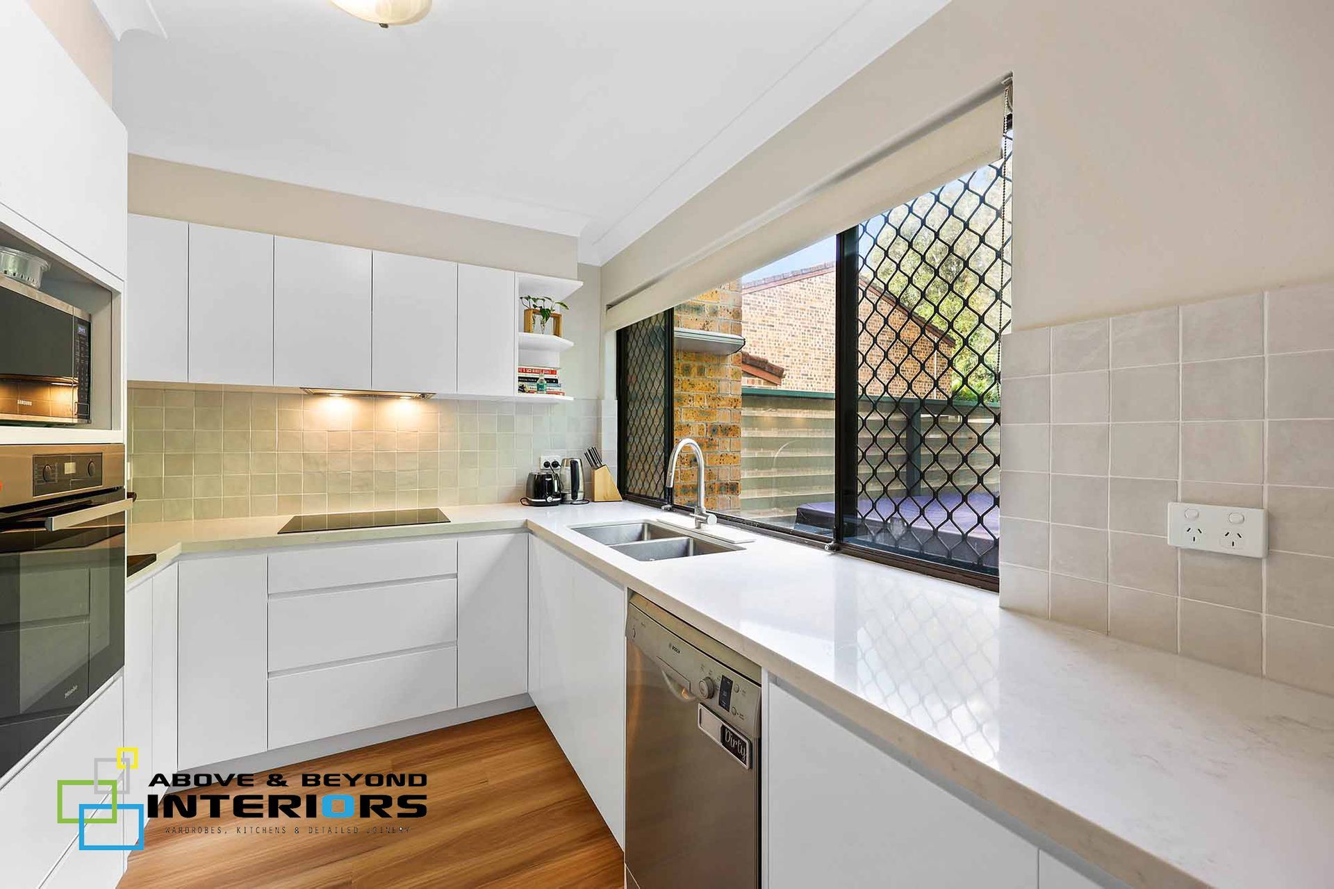 A Bright White Shaped Kitchen with Wooden Floor — Above & Beyond Interiors in Smeaton Grange, NSW