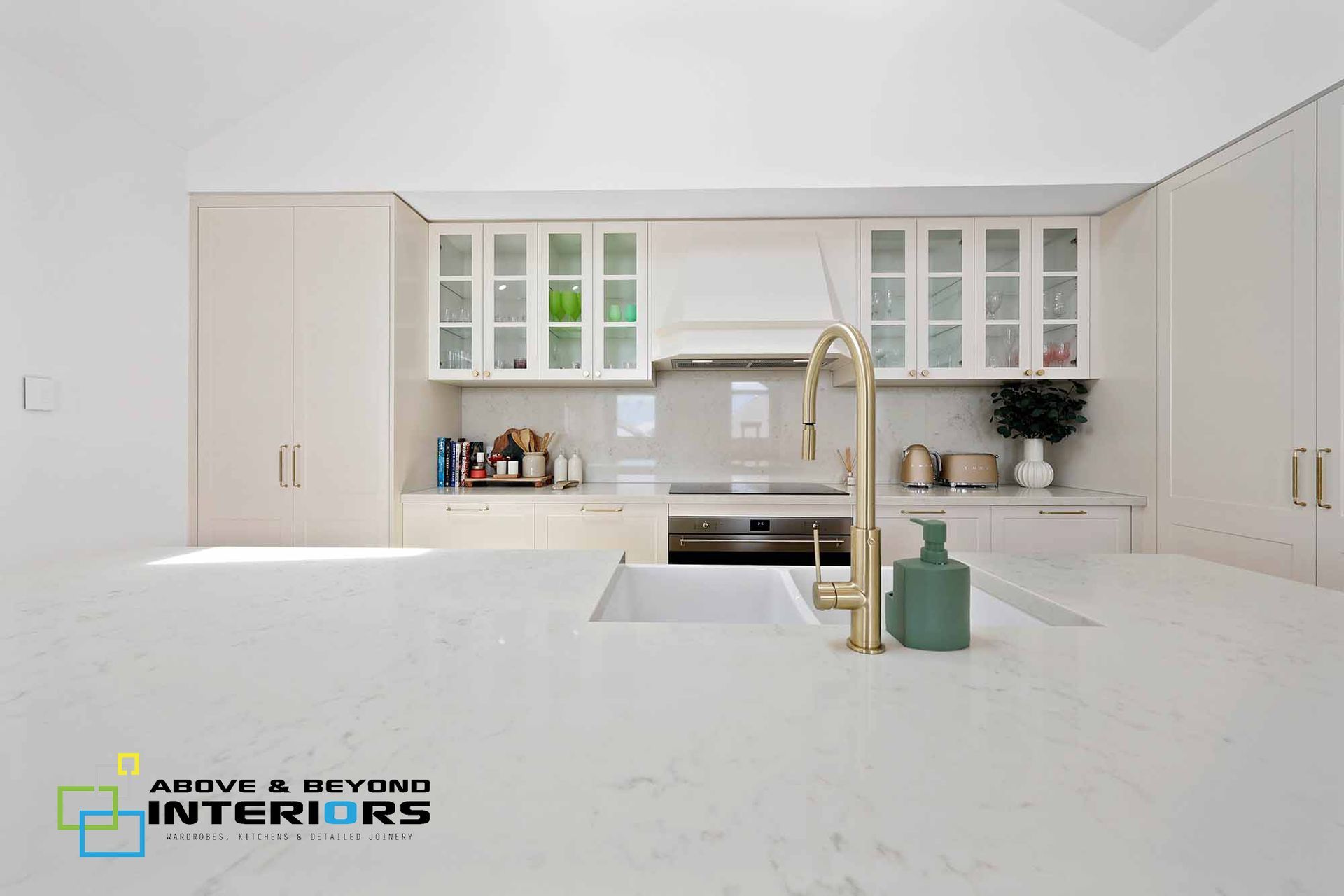 Bright White Modern Kitchen with A Large Island, Gold Faucet, and Glass-Front Cabinets — Above & Beyond Interiors in Smeaton Grange, NSW