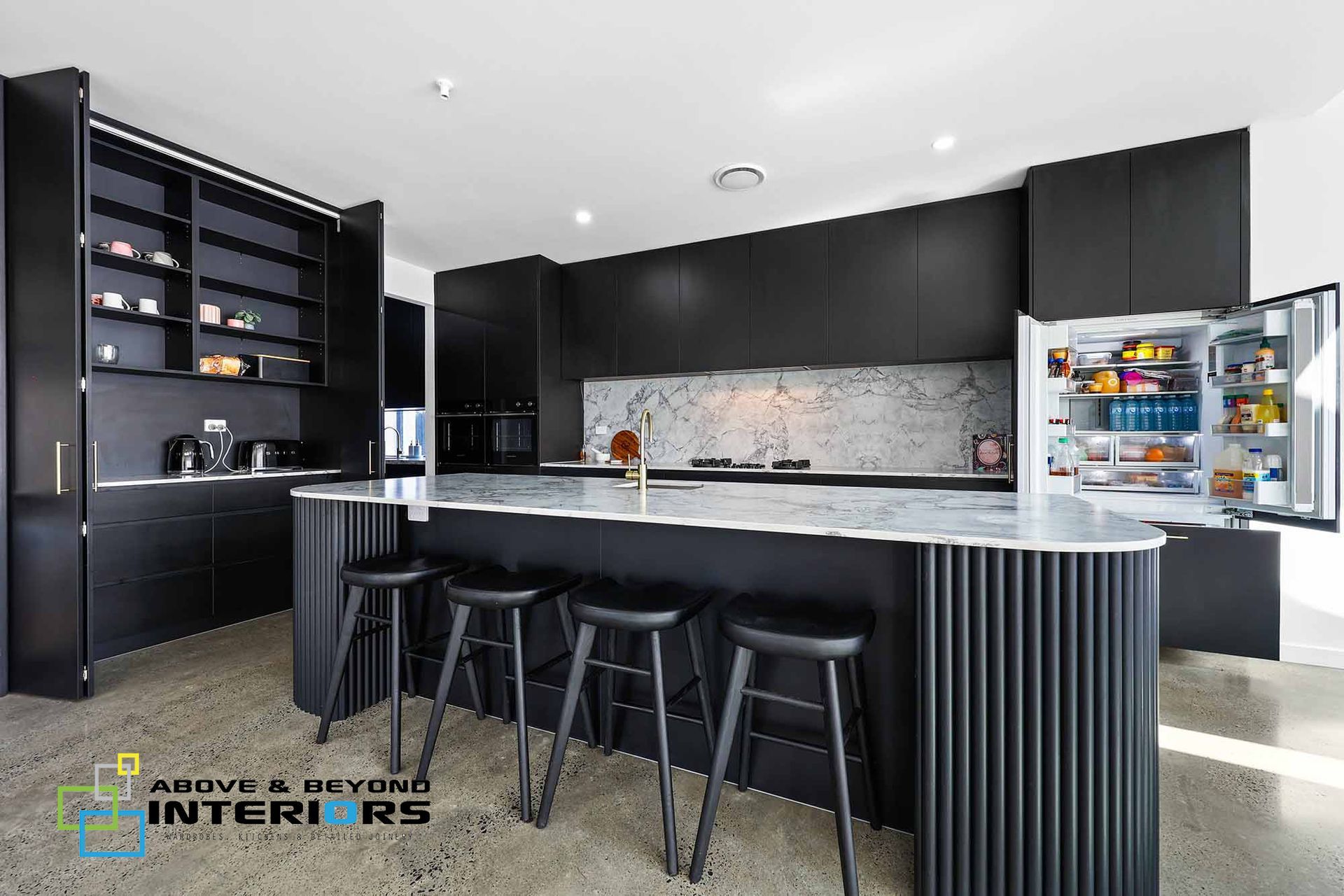 Modern Black Kitchen with Island, Stools, and Open Refrigerator in A Bright Room — Above & Beyond Interiors in Smeaton Grange, NSW
