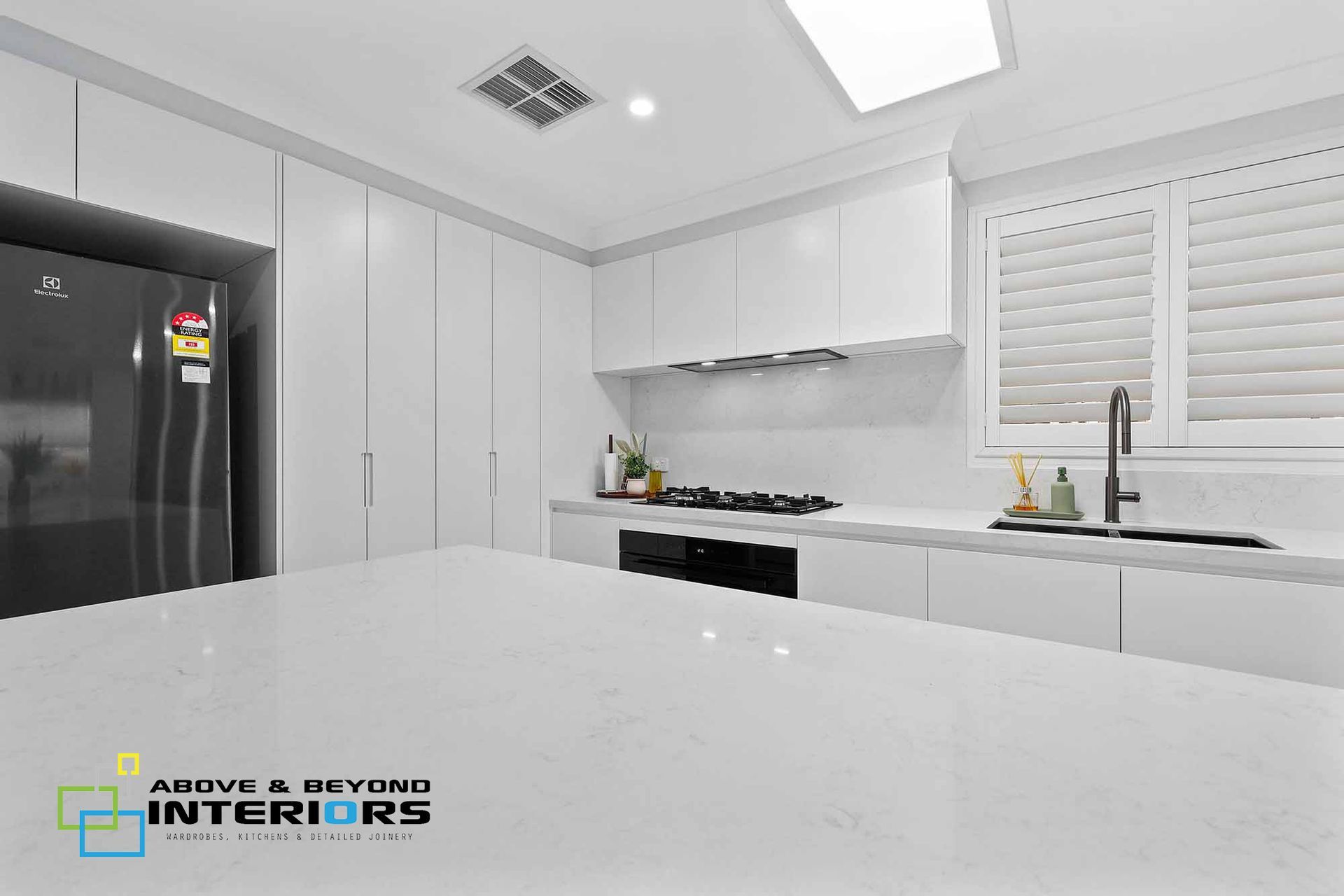 Bright Modern White Kitchen with Black Refrigerator, and Window Blinds — Above & Beyond Interiors in Smeaton Grange, NSW