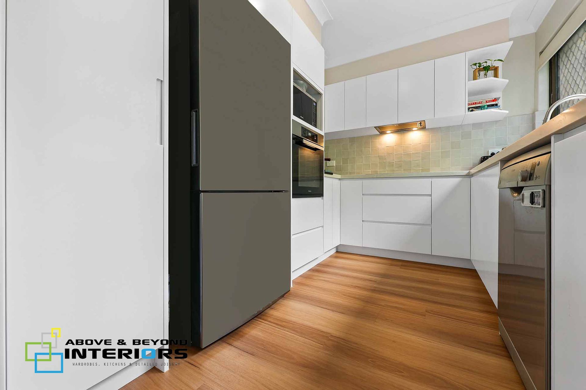 Modern White Kitchen with Wood Floors, Black Appliances, and Cabinet — Above & Beyond Interiors in Smeaton Grange, NSW