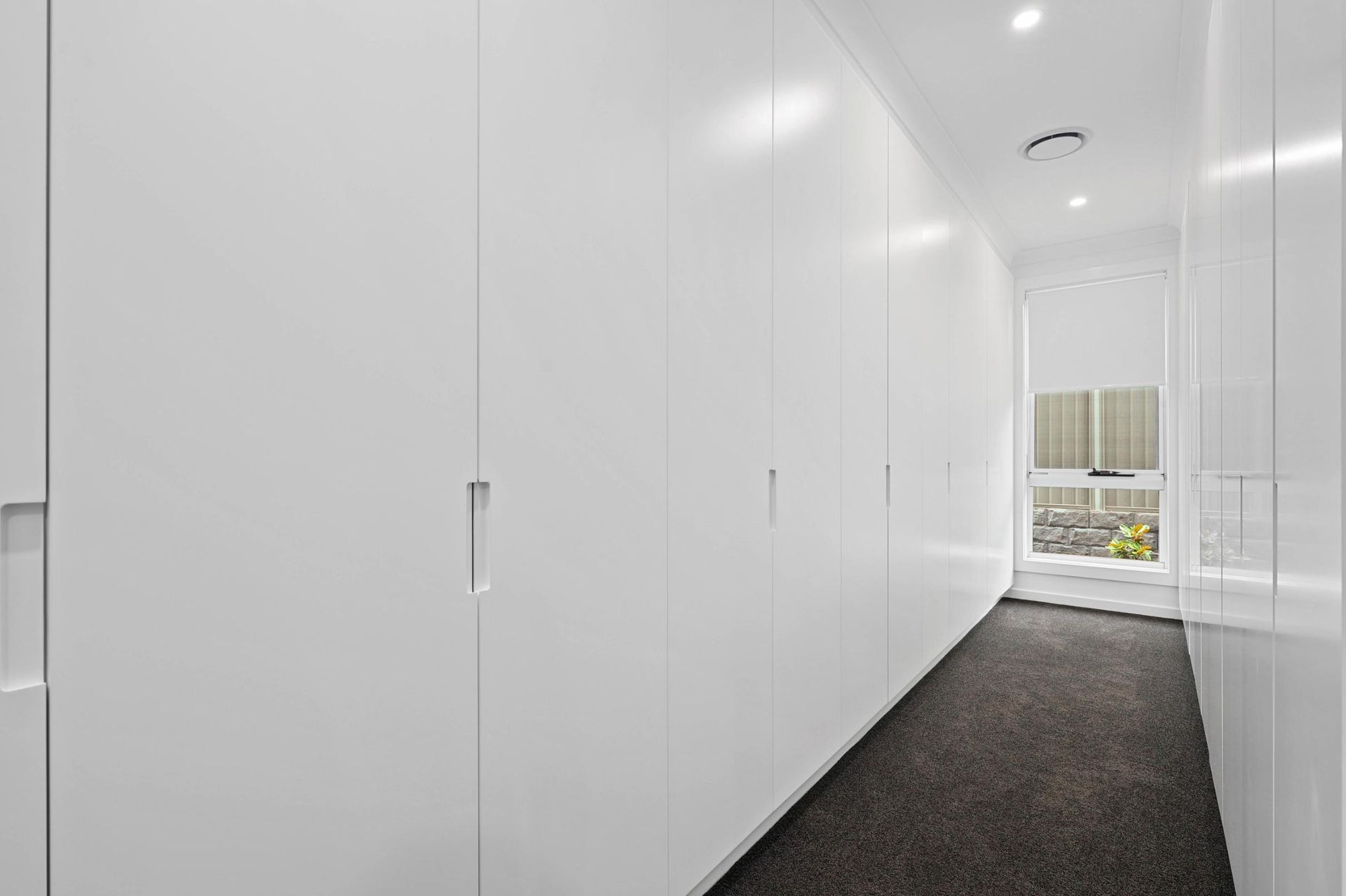 Narrow White Hallway With Built-in Cabinets and Dark Carpet — Above & Beyond Interiors in Smeaton Grange, NSW