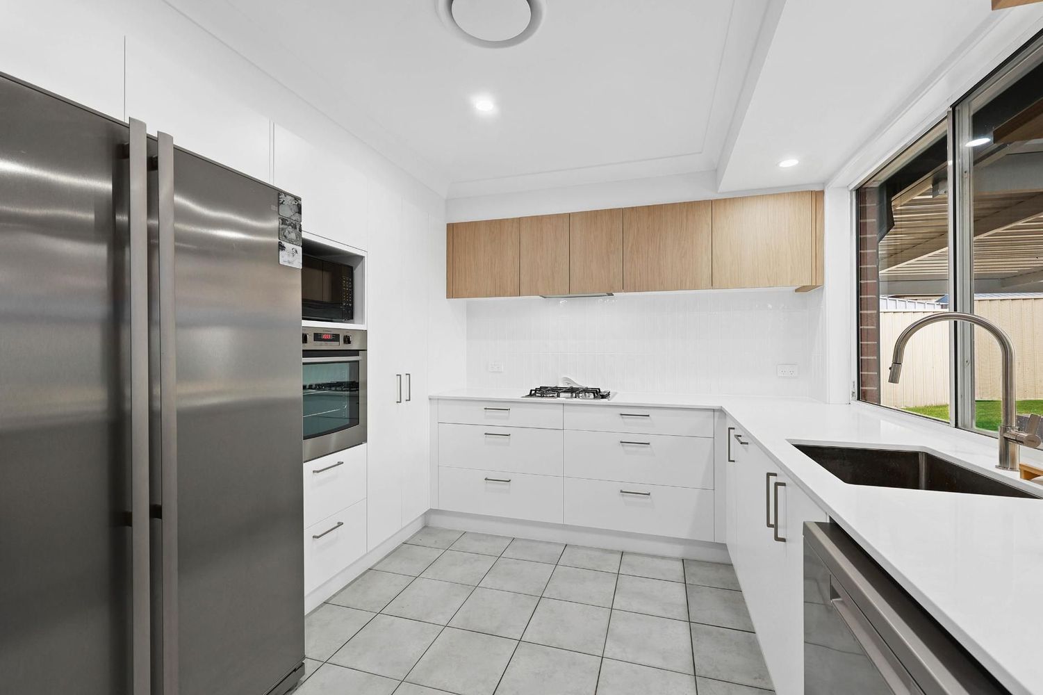 Modern White Kitchen With Stainless Steel Fridge — Above & Beyond Interiors in Smeaton Grange, NSW