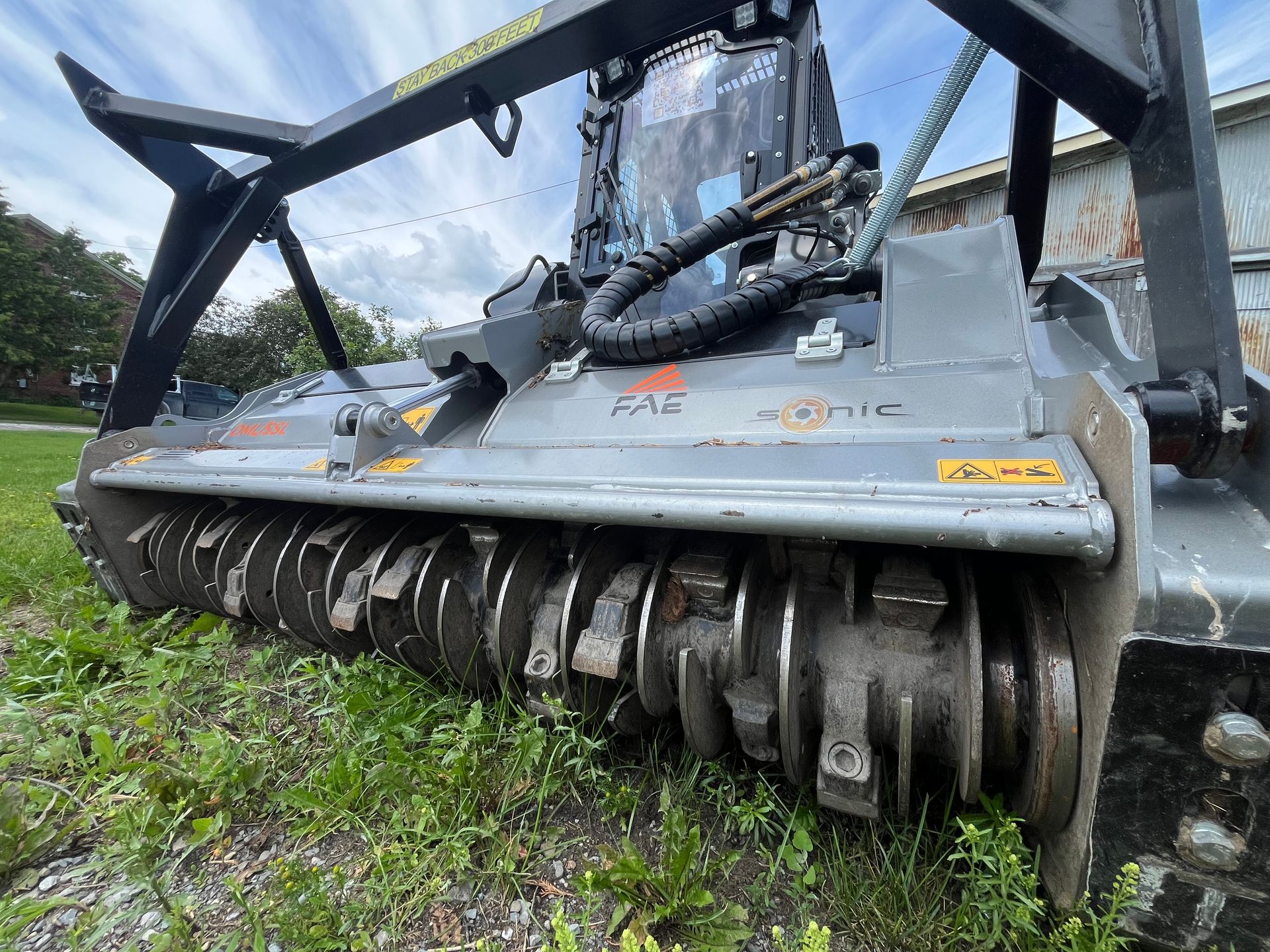 Heavy black forestry mulcher with spinning drum, mounted on gray machine in a grassy field.