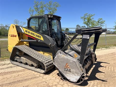 Yellow and black New Holland skid steer loader with front grapple on a dirt lot under a blue sky