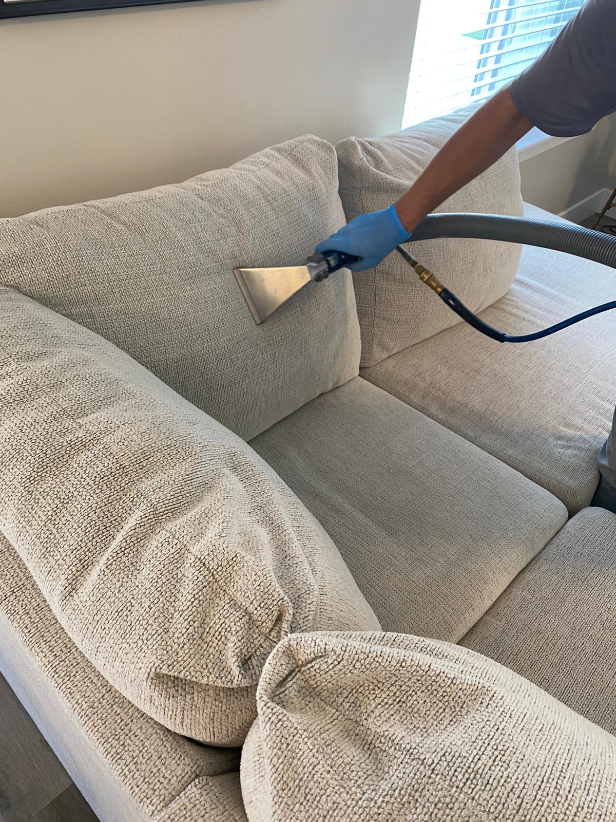 A person is cleaning a couch with a vacuum cleaner.
