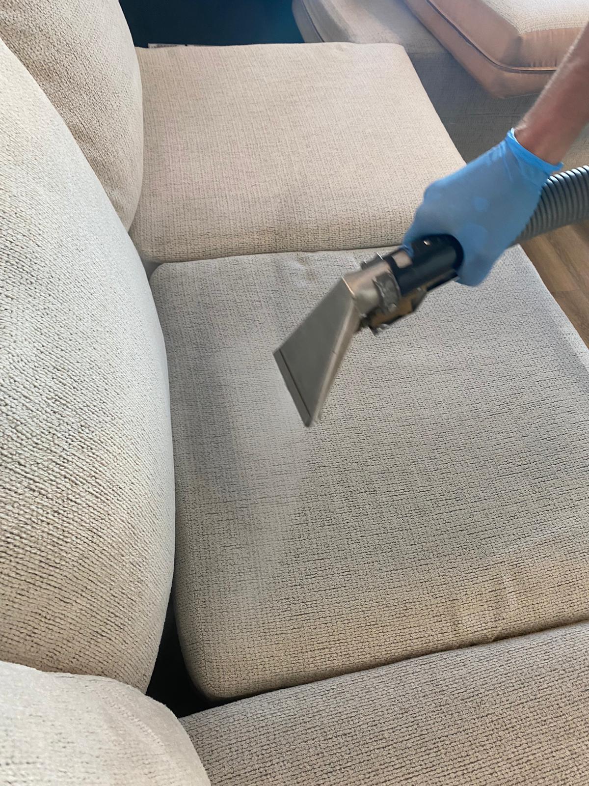A person is cleaning a couch with a vacuum cleaner.