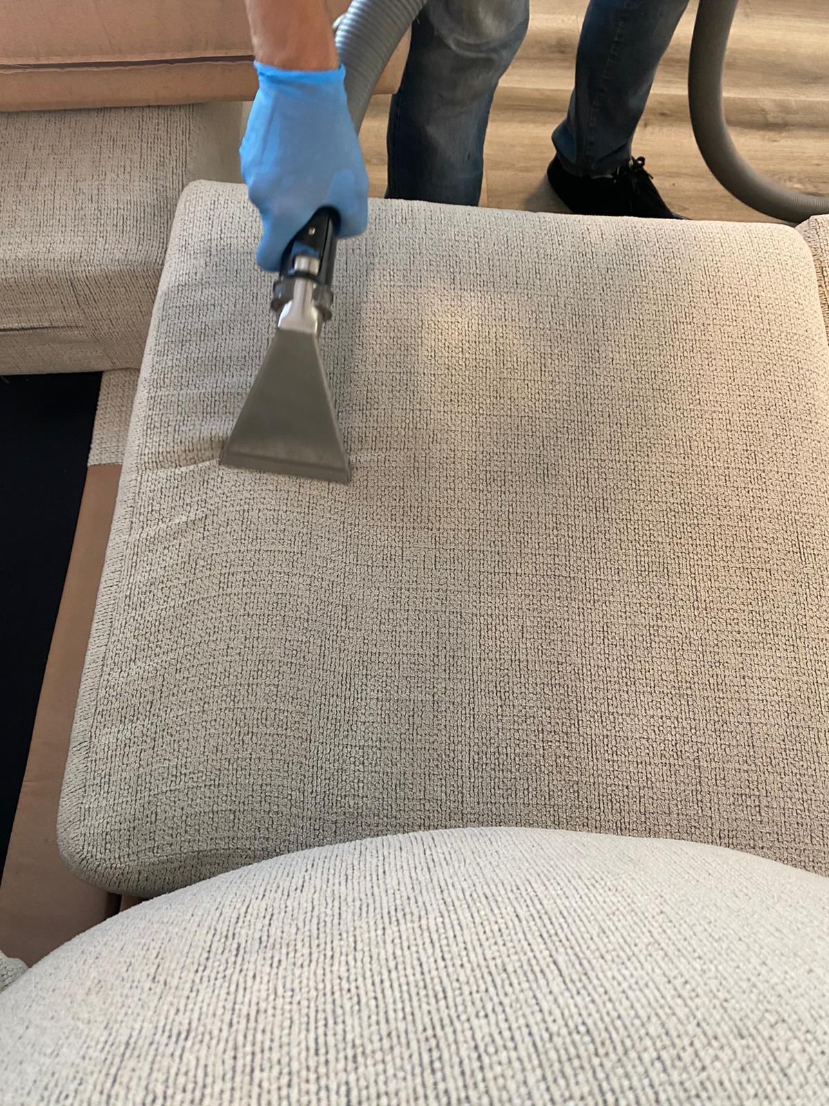 A person is cleaning a couch with a vacuum cleaner.