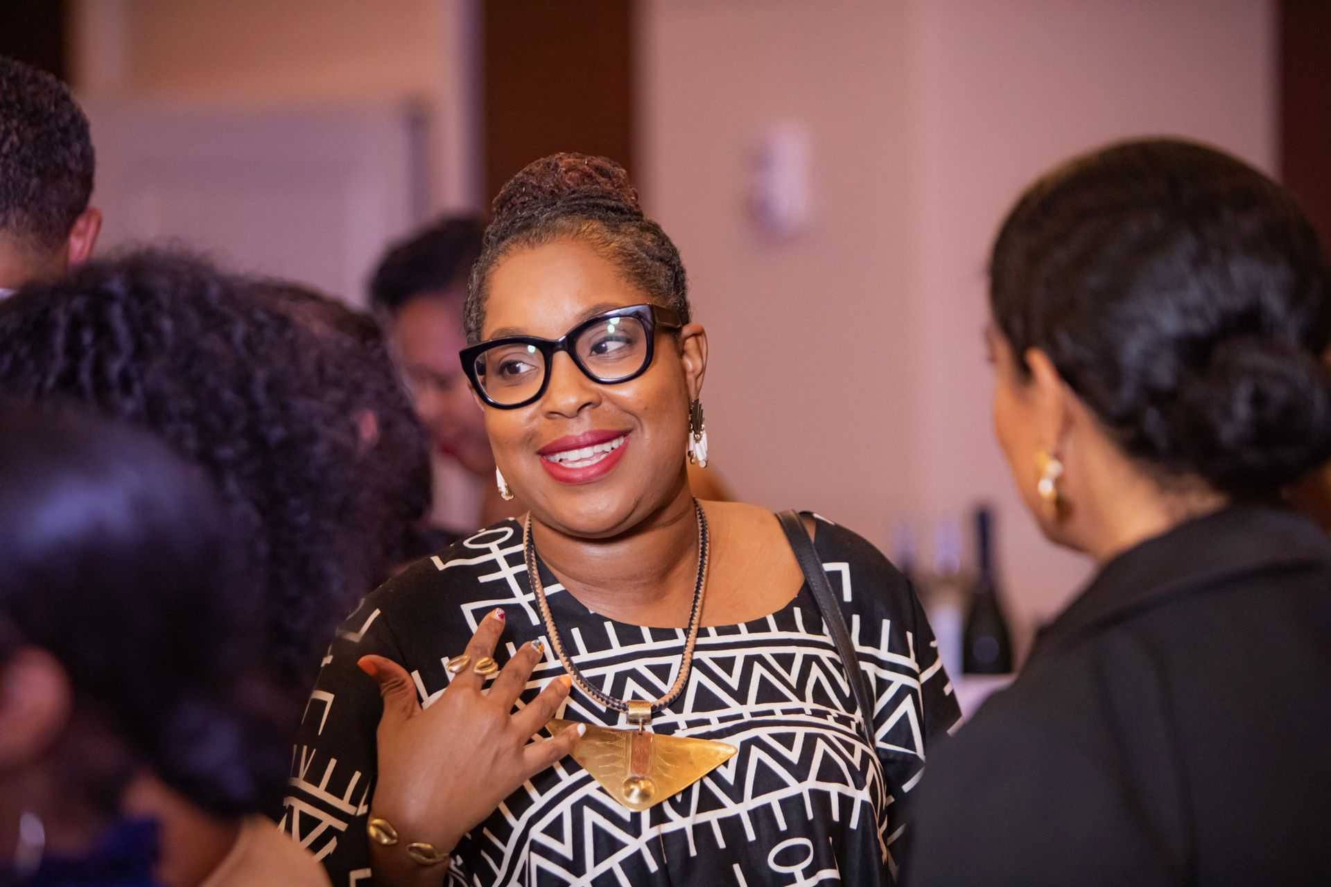A woman wearing glasses is smiling while talking to another woman.
