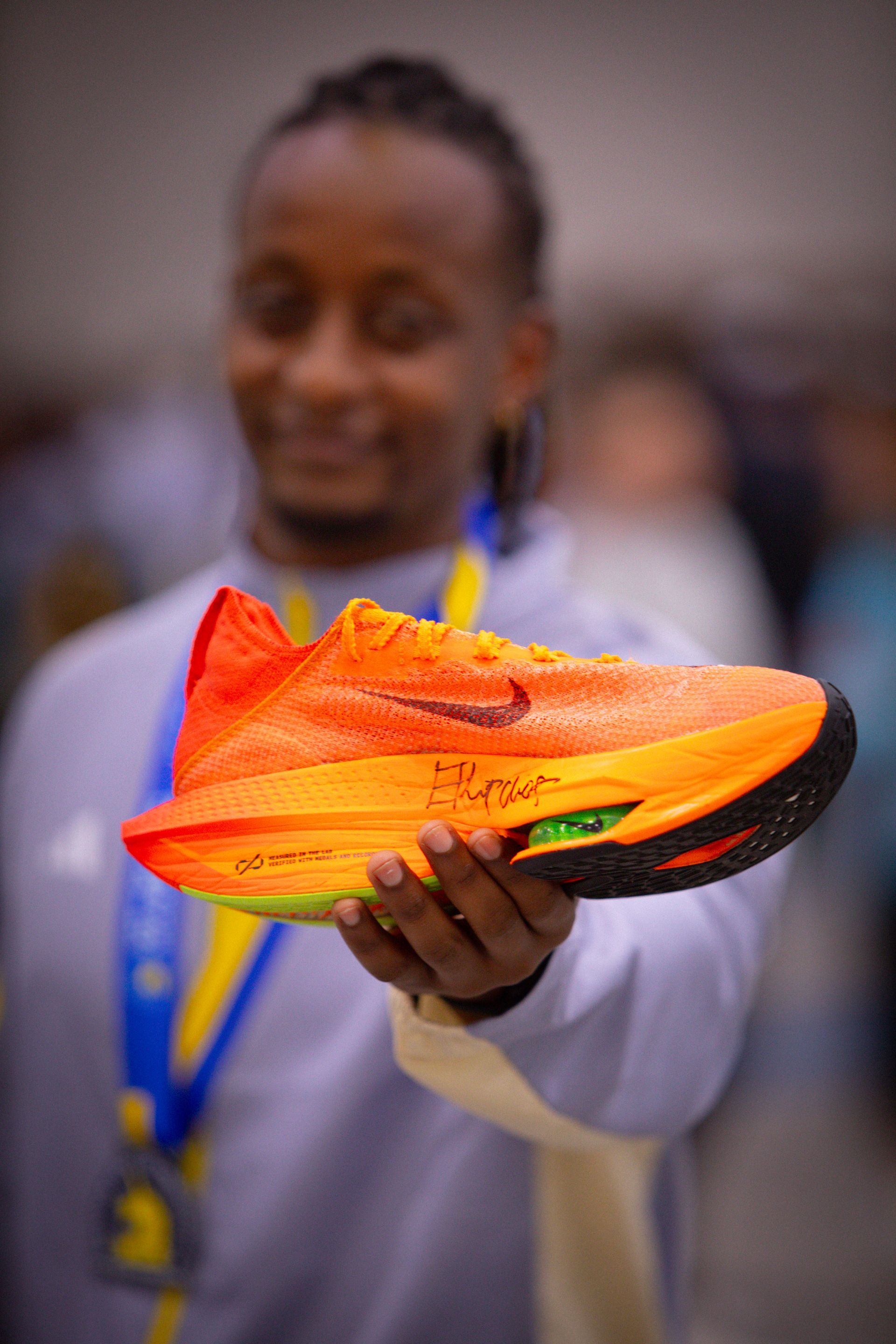 A man is holding a pair of orange nike shoes in his hands.