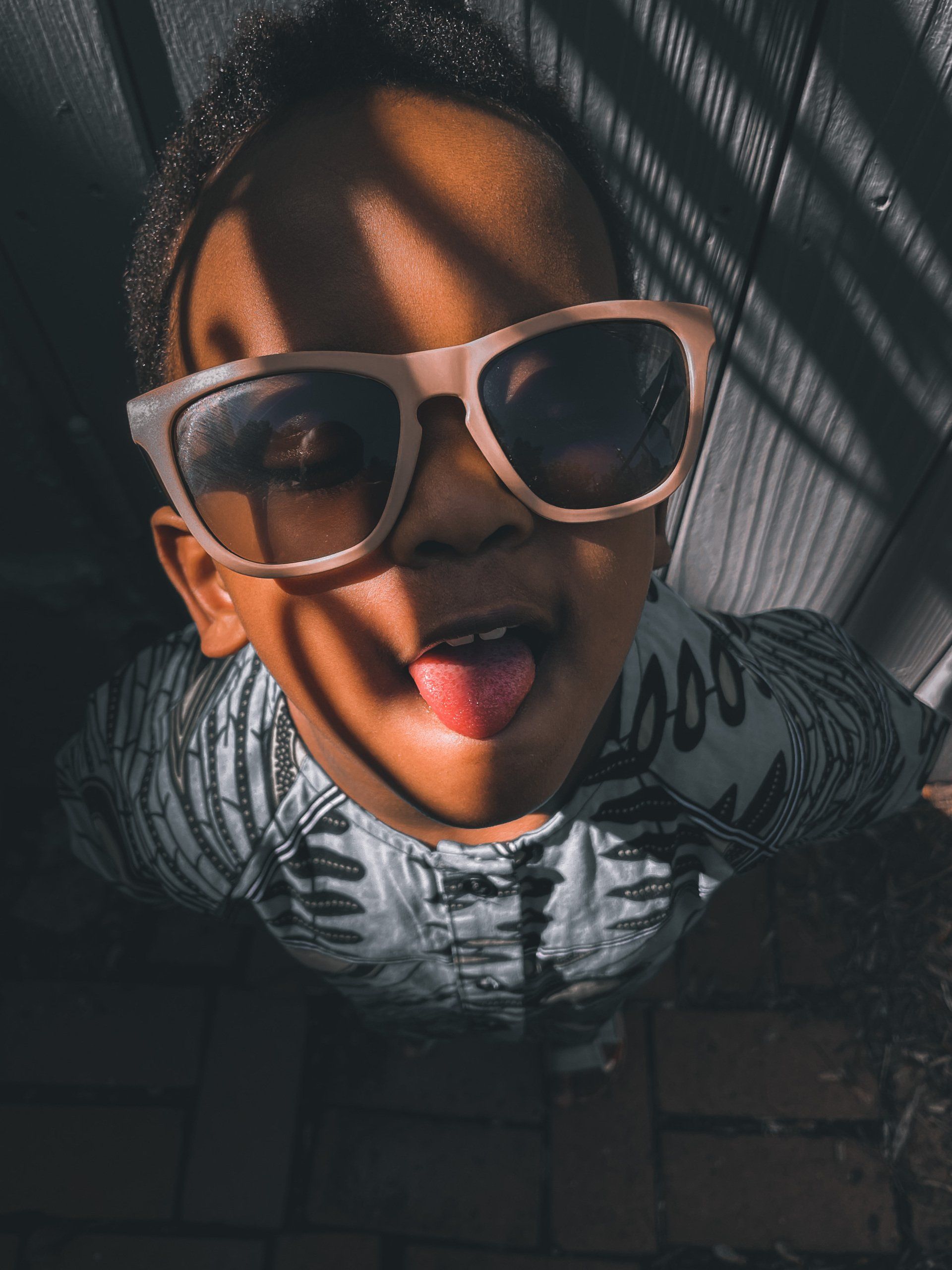A young boy wearing sunglasses is sticking his tongue out.
