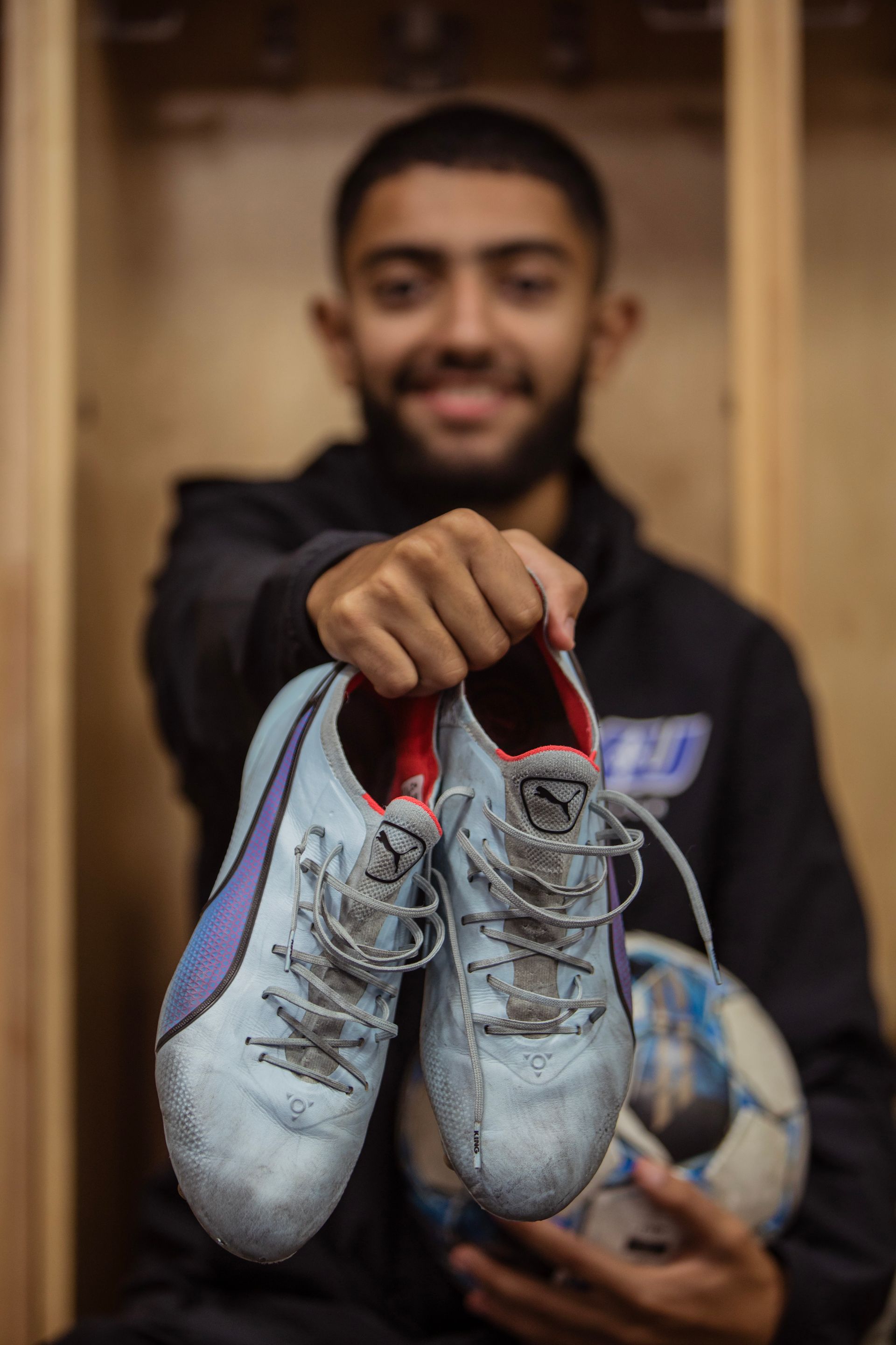 A man is holding a pair of soccer cleats and a soccer ball.