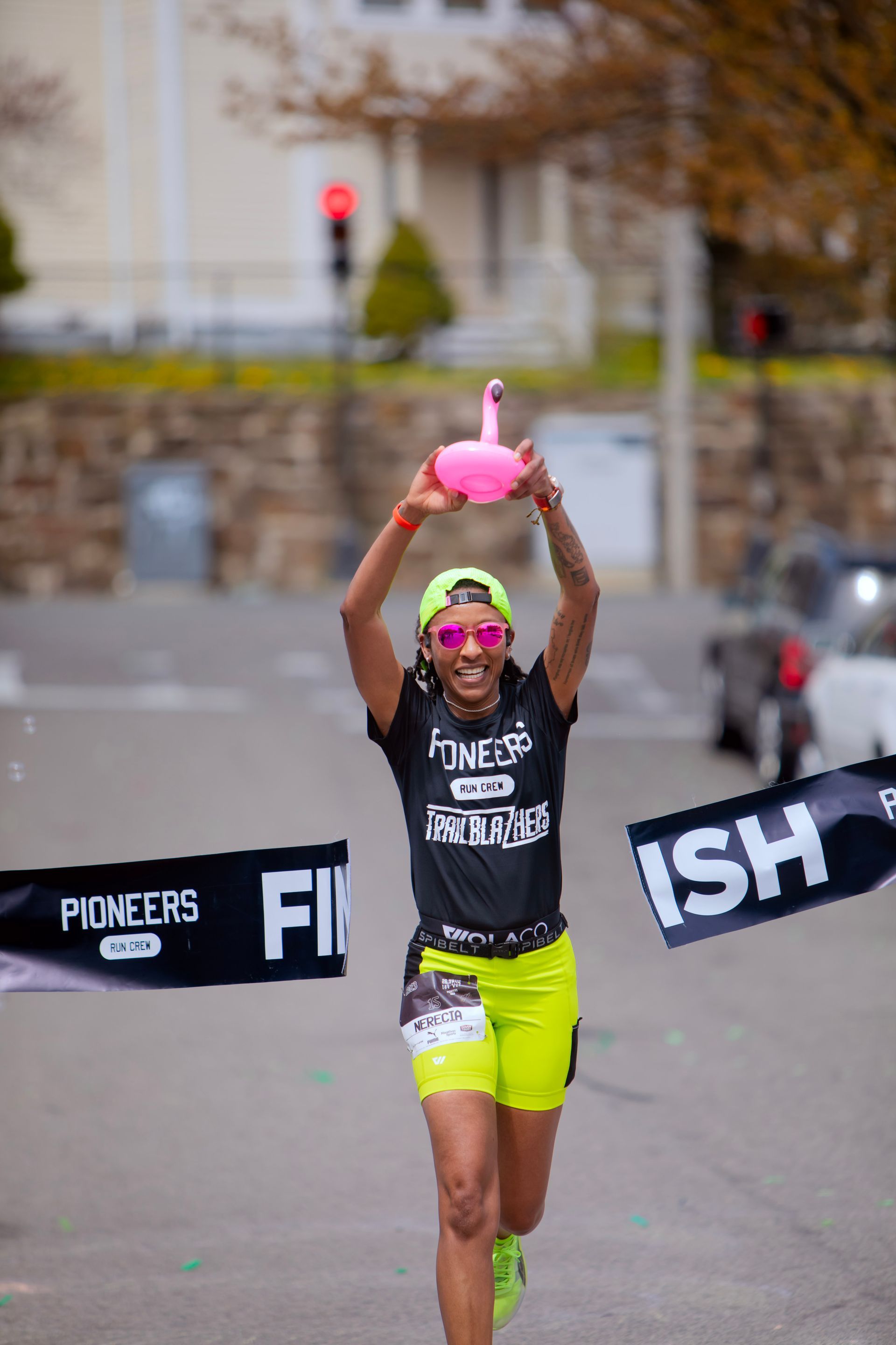 A woman is running a marathon and holding a pink flamingo balloon.