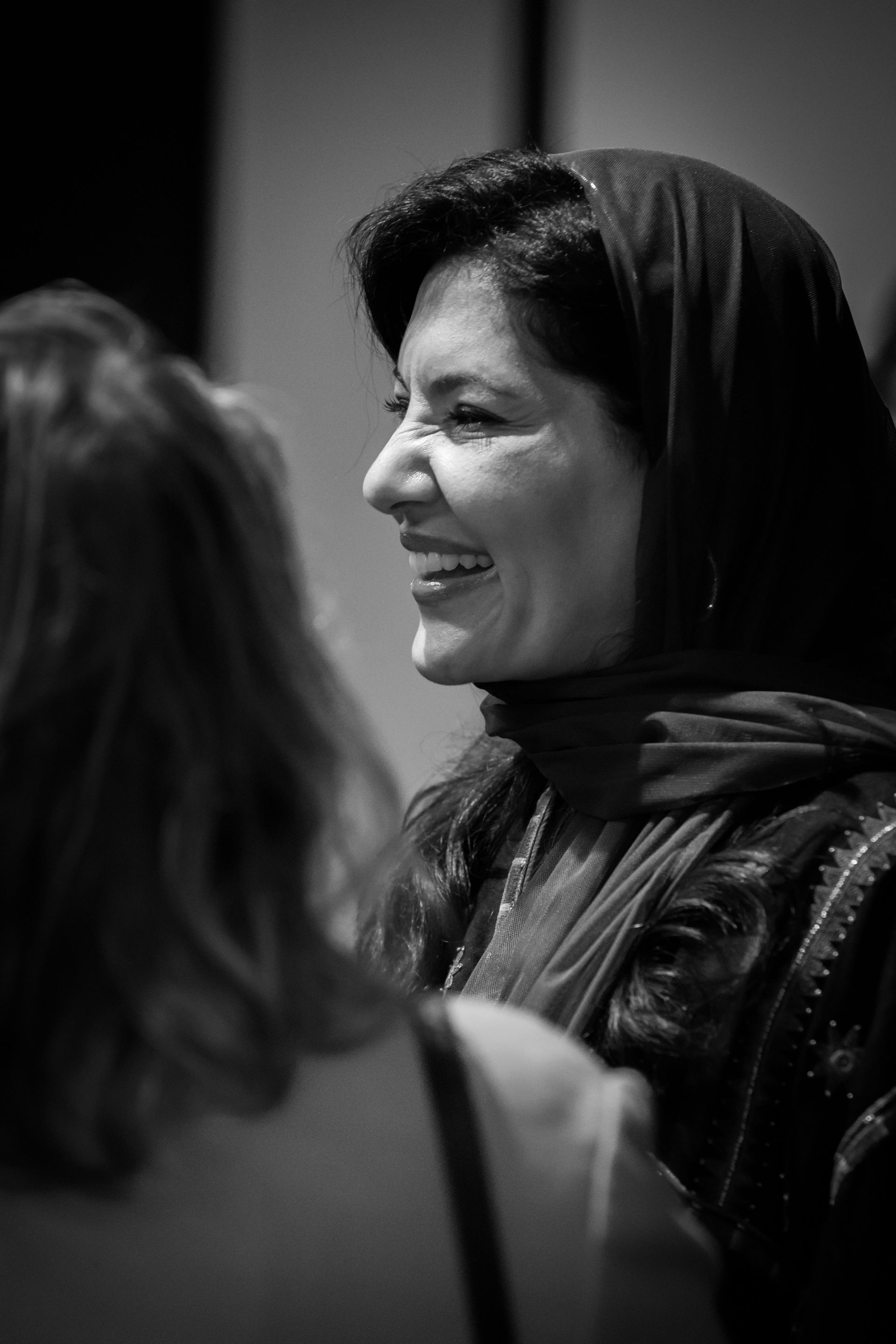 A black and white photo of a woman wearing a scarf talking to another woman.