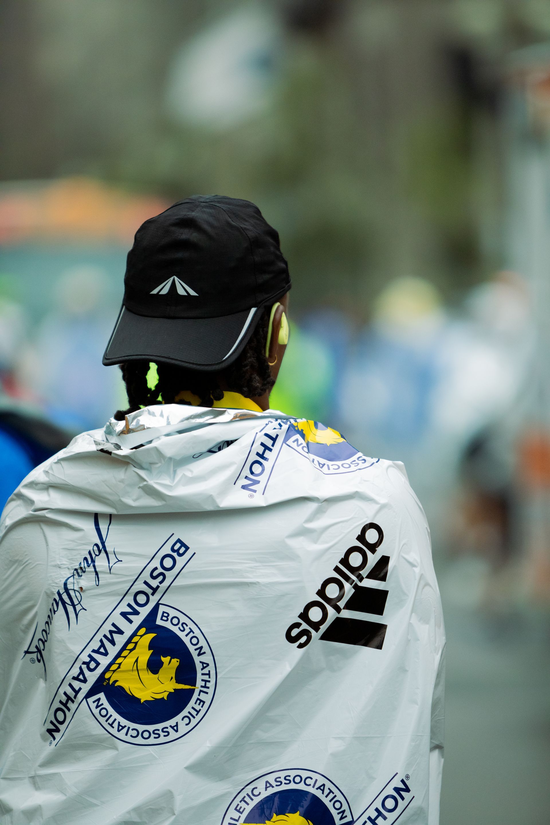 A man wearing a black hat and a white Adidas cape walks down the street in Boston