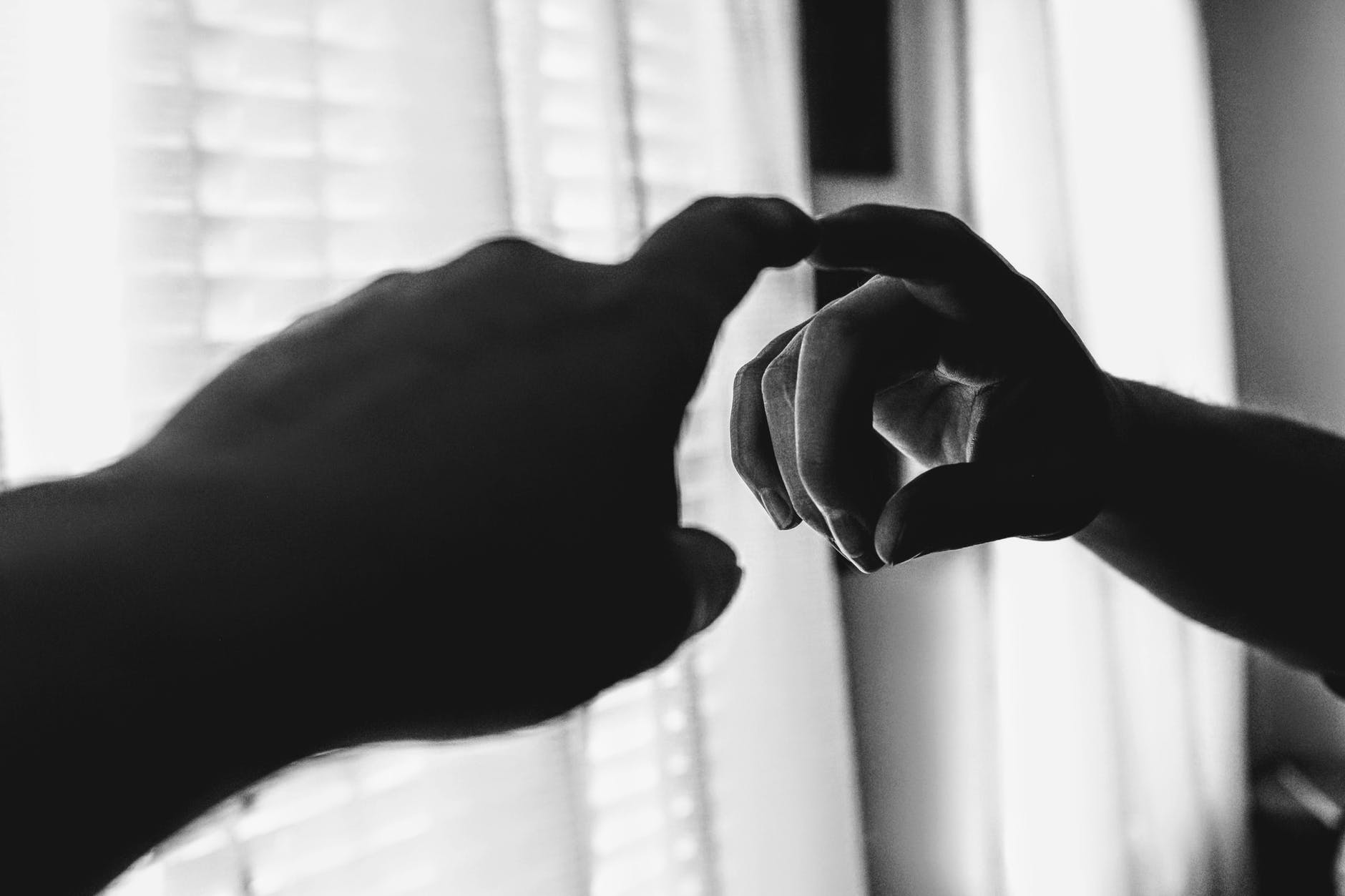 A person is making a heart shape with their hands in front of a window.