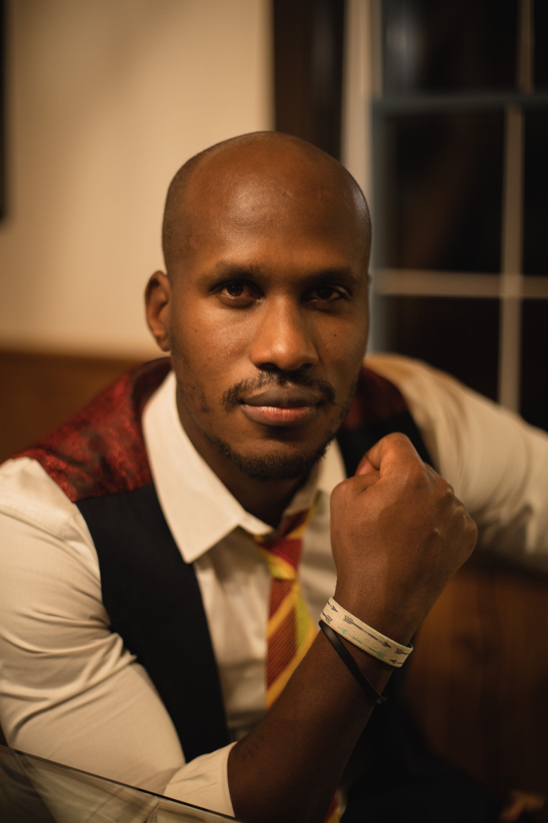 A bald man wearing a vest and tie is sitting on a couch.