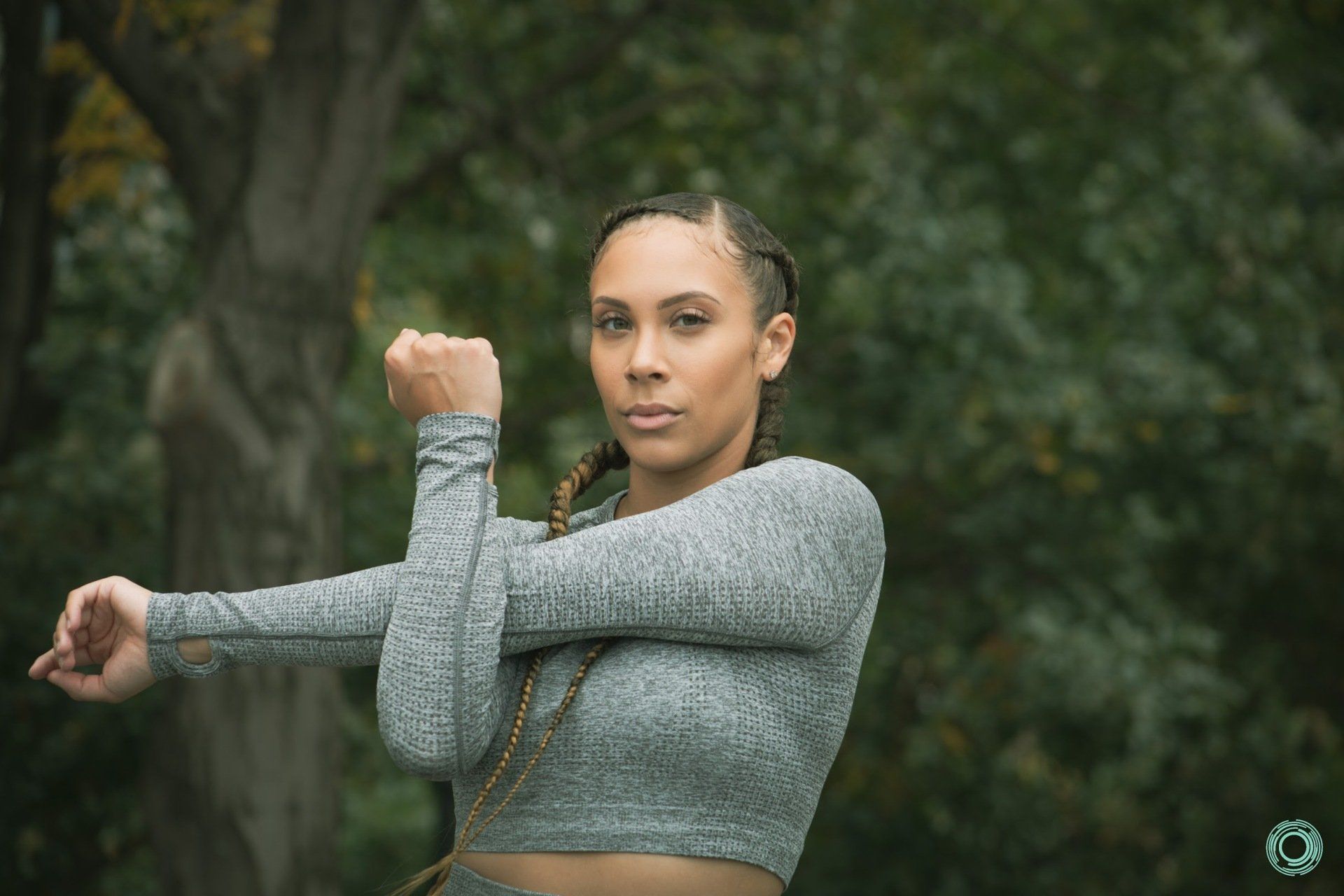 A woman in a gray crop top is stretching her arms in a park.
