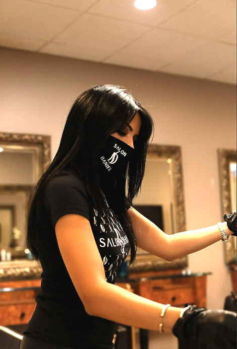 A woman wearing a mask and a shirt that says ' Salon Daniel ' on it