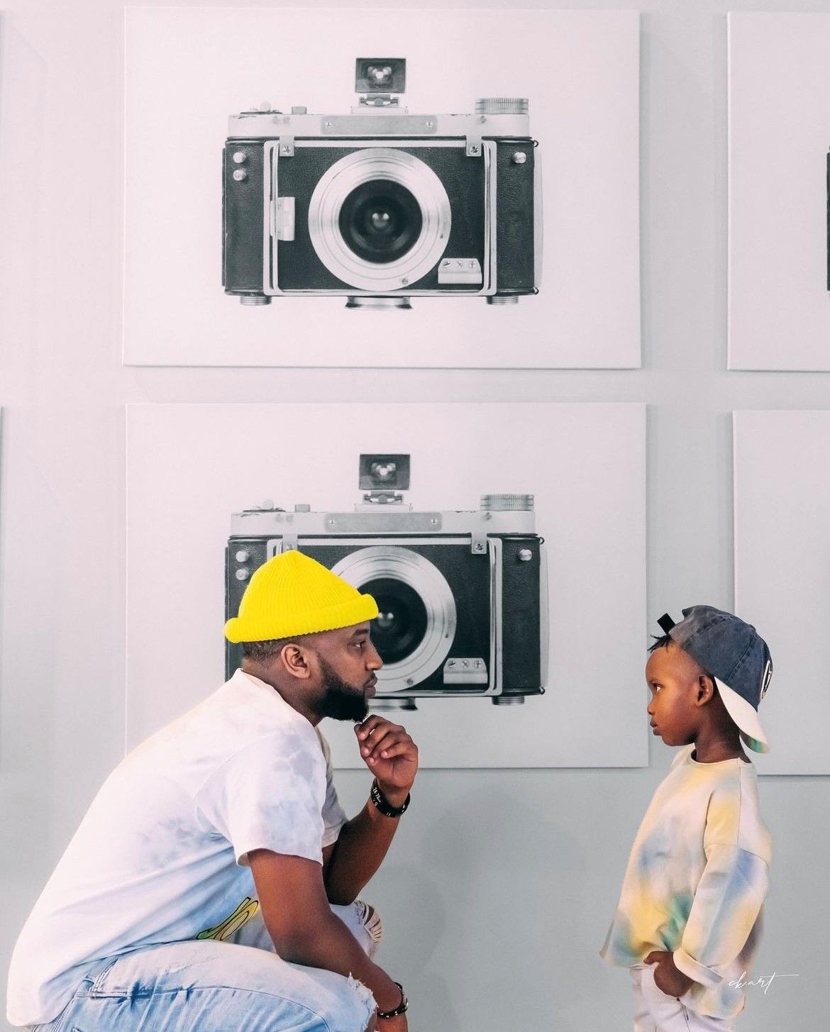 A man and a child are standing in front of a wall with pictures of cameras on it.